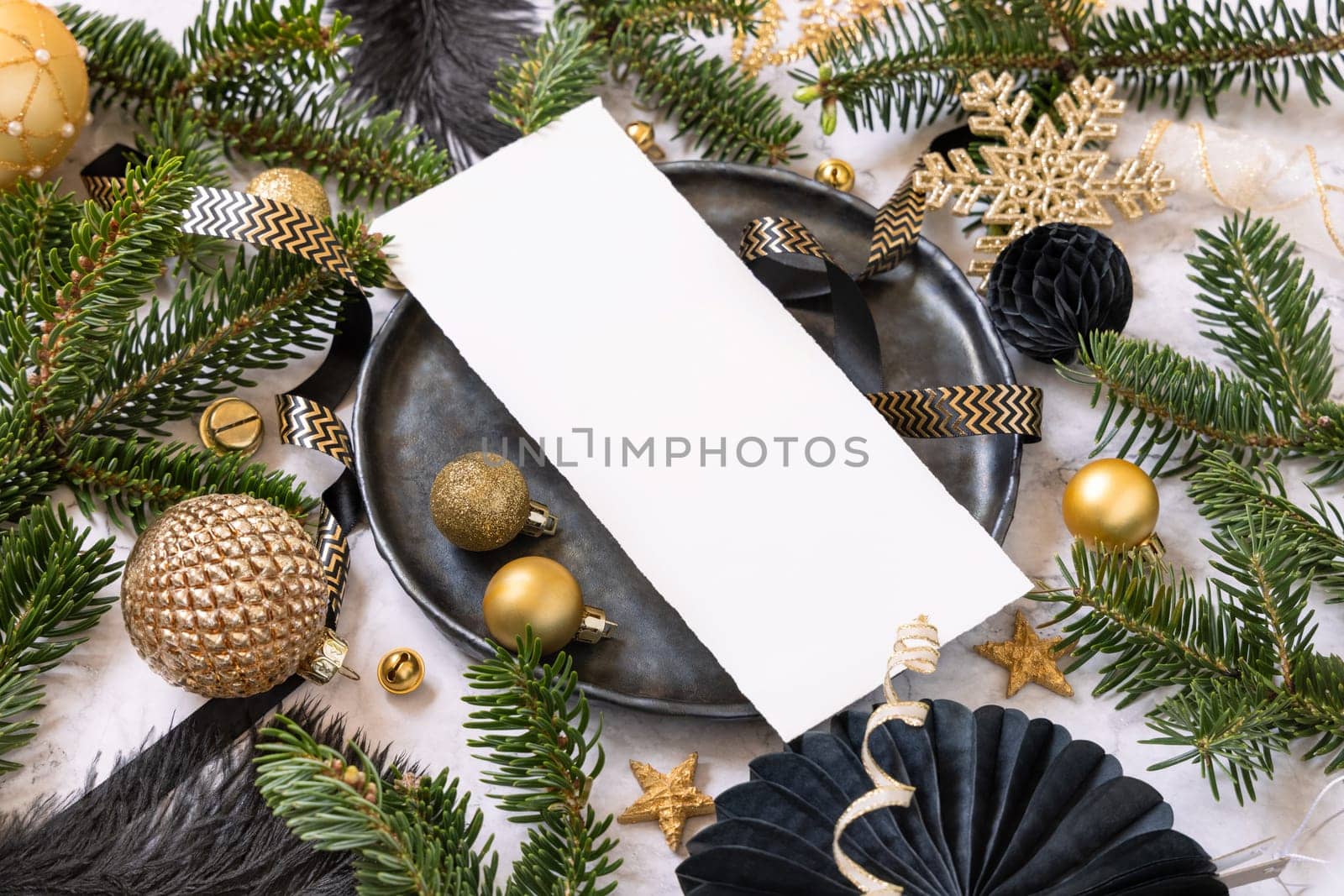 Black and golden Table setting with ornaments and fir tree branches, card mockup. Christmas or New Year menu on marble table close up, copy space. Winter season, restaurant holiday catering