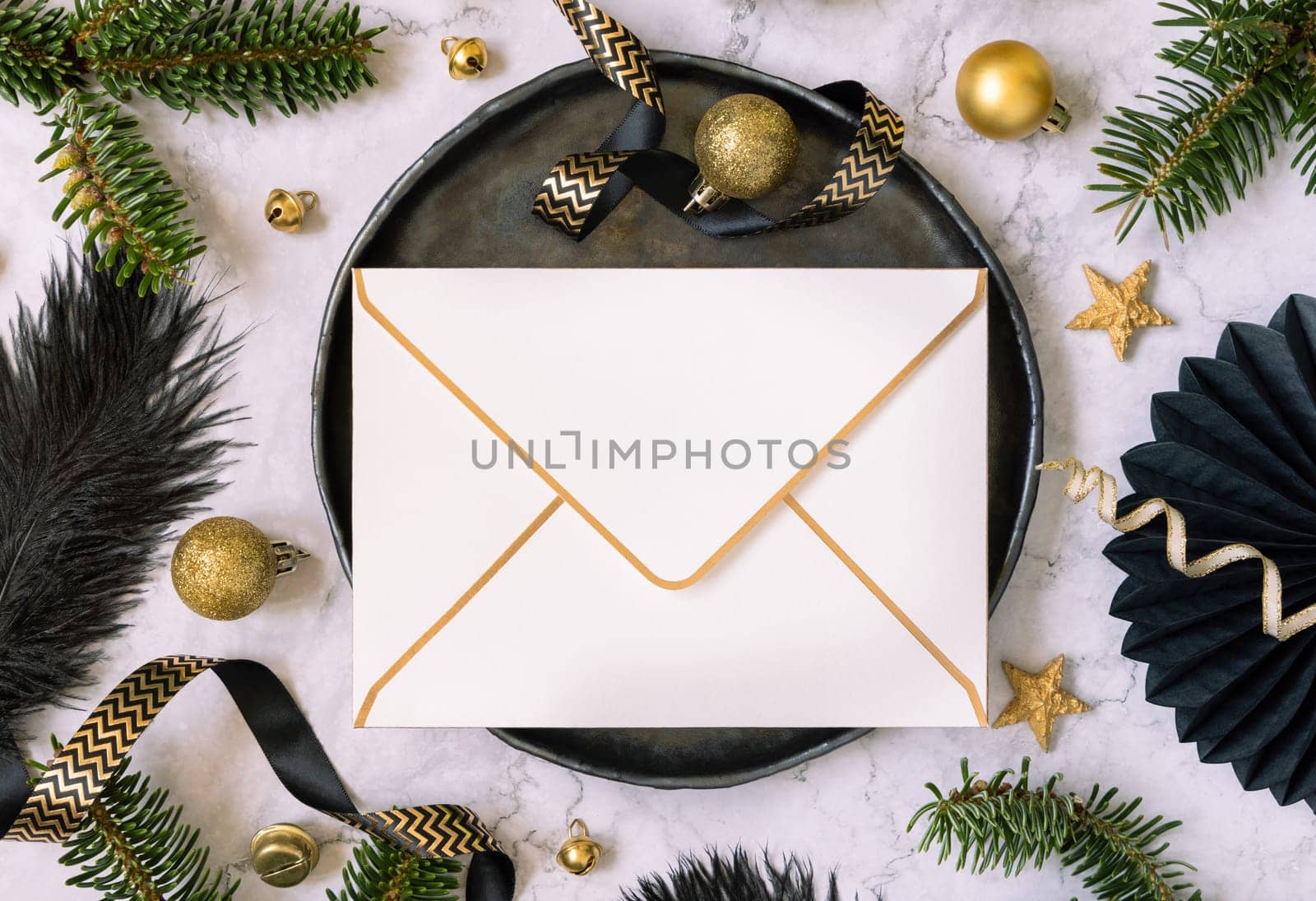 Black and golden Table setting with ornaments and fir tree branches top view, envelope mockup. Christmas or New Year atmospheric composition on marble table, copy space.