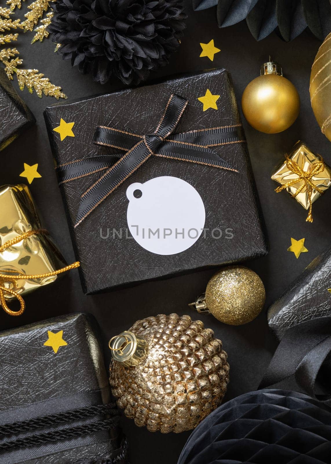Black and golden Christmas Gift Boxes with a bow and ornaments close up, round paper gift tag mockup, copy space. Dark winter composition with blank label card for Christmas, New Year, Birthday, Anniversary