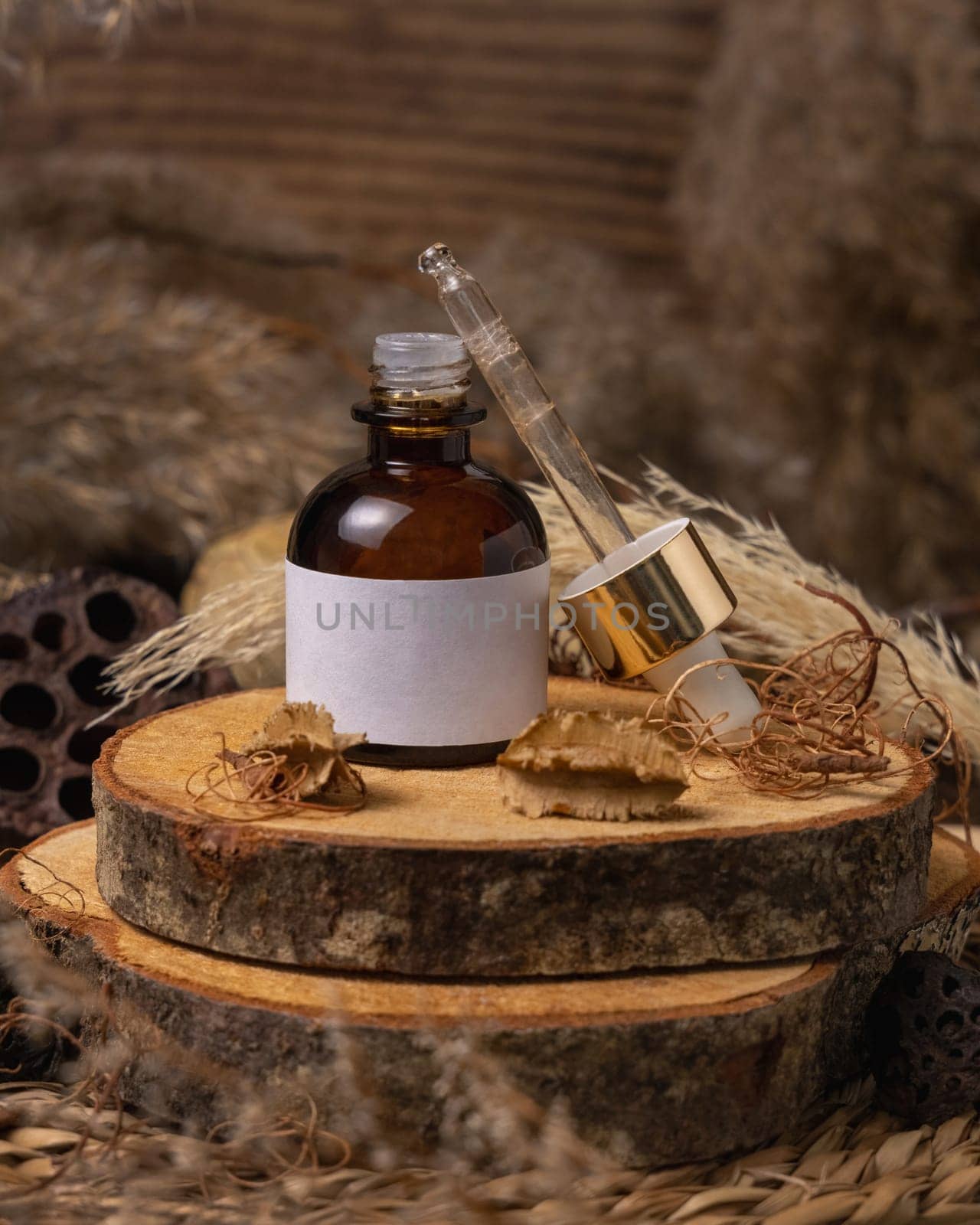 Opened glass bottle on wood near natural boho decorations close up, cosmetics label mockup. Eco friendly Skincare beauty product, serum or essence. Bohemian composition with dried leaves and flowers.