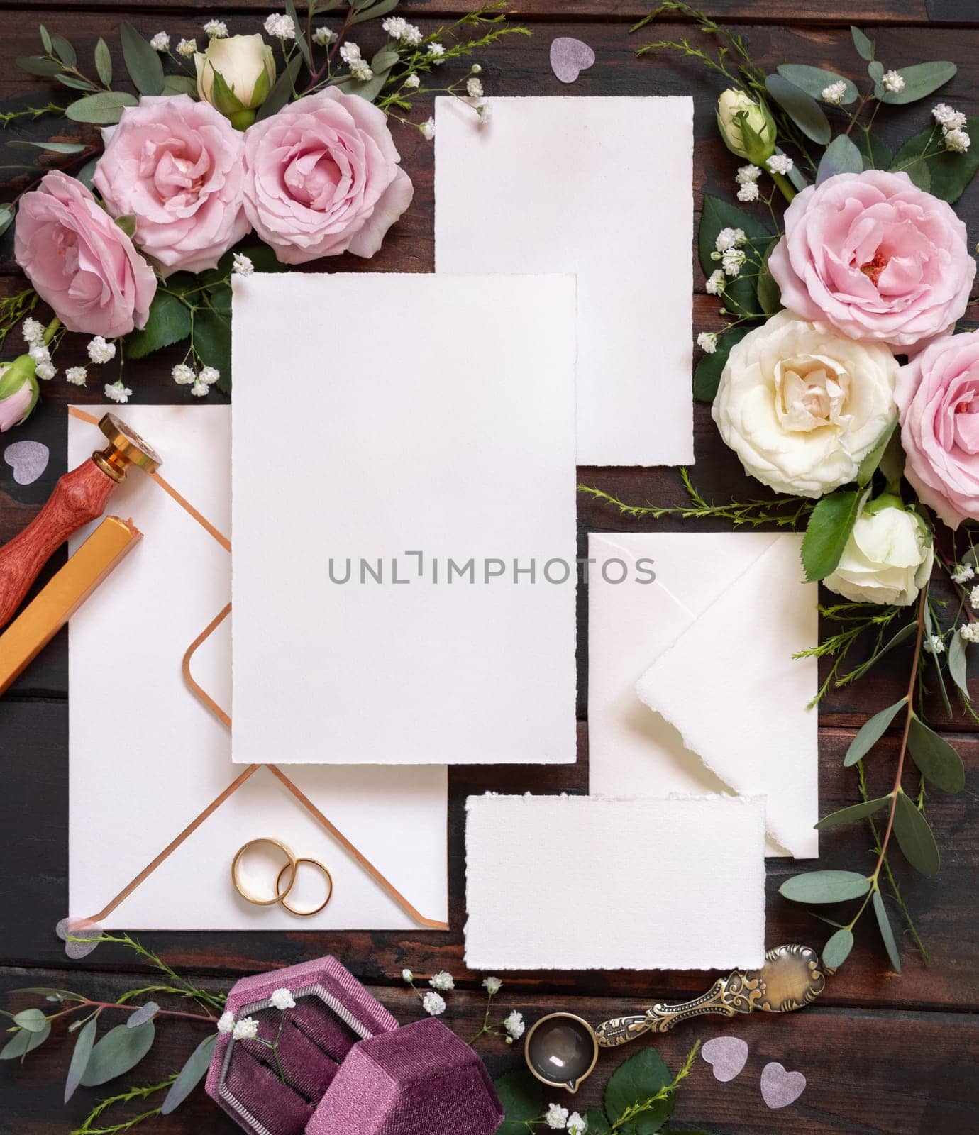 Cards and envelope between pink and cream roses on brown wood top view, wedding mockup. Romantic scene with cards, envelope, rings and pastel flowers flat lay. Valentines, Spring or Mothers day concept