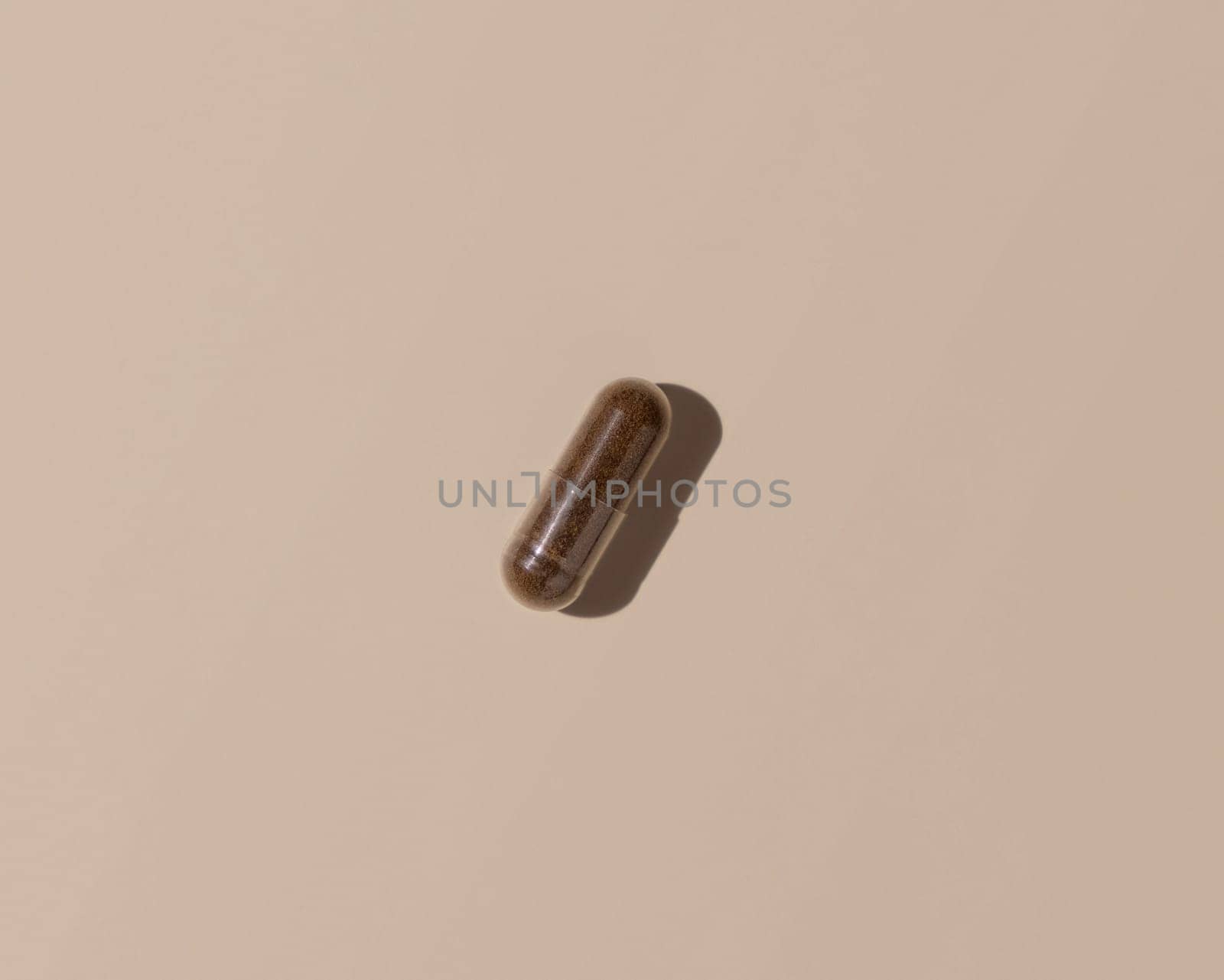Brown medical capsule on light beige top view, hard shadows. Preventive medicine and healthcare, taking dietary supplements and vitamins. Minimal composition