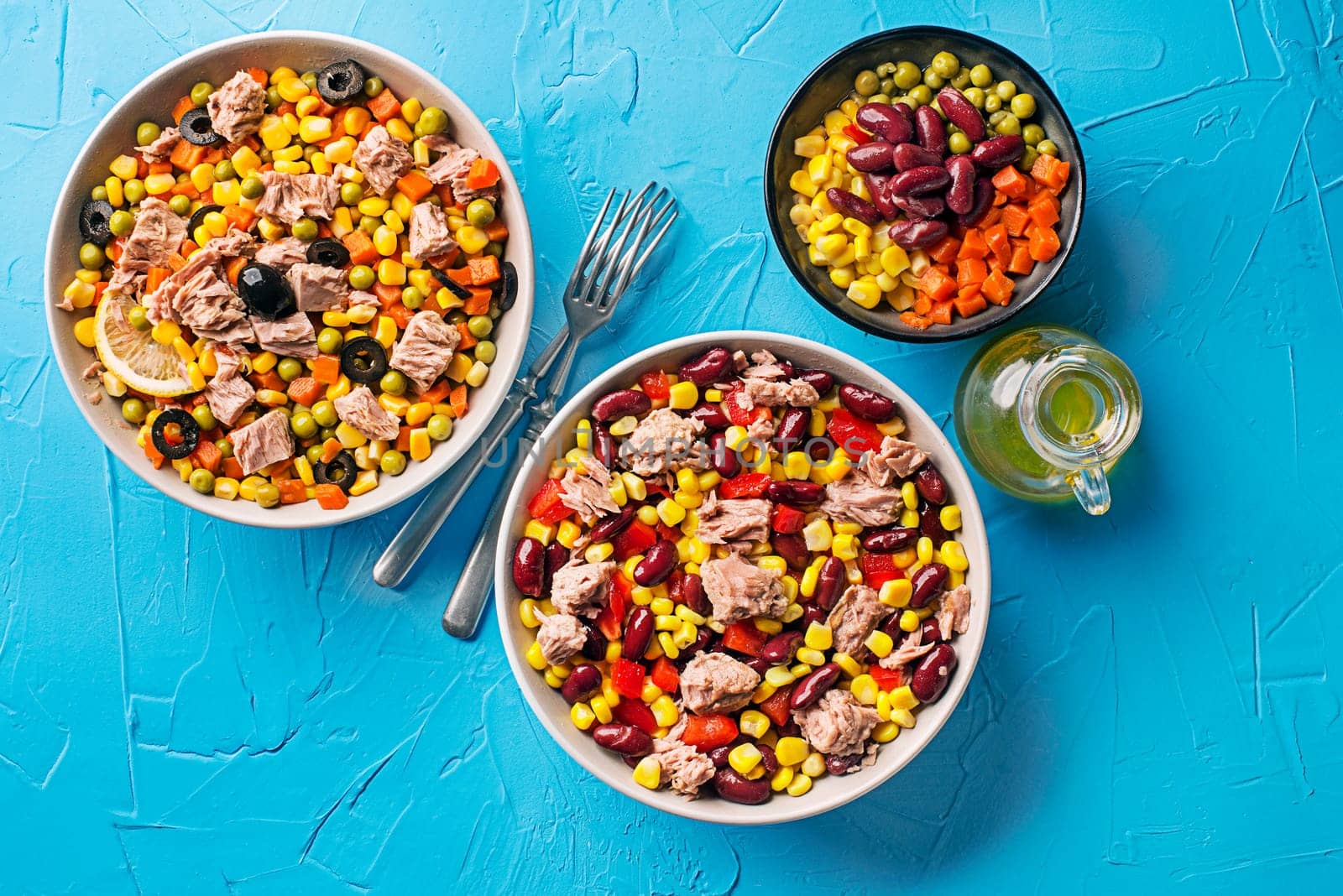 Healthy mixed tuna salads with corns, carrots, peas, beans, peppers and olives on blue table background. Mexican corn salad.