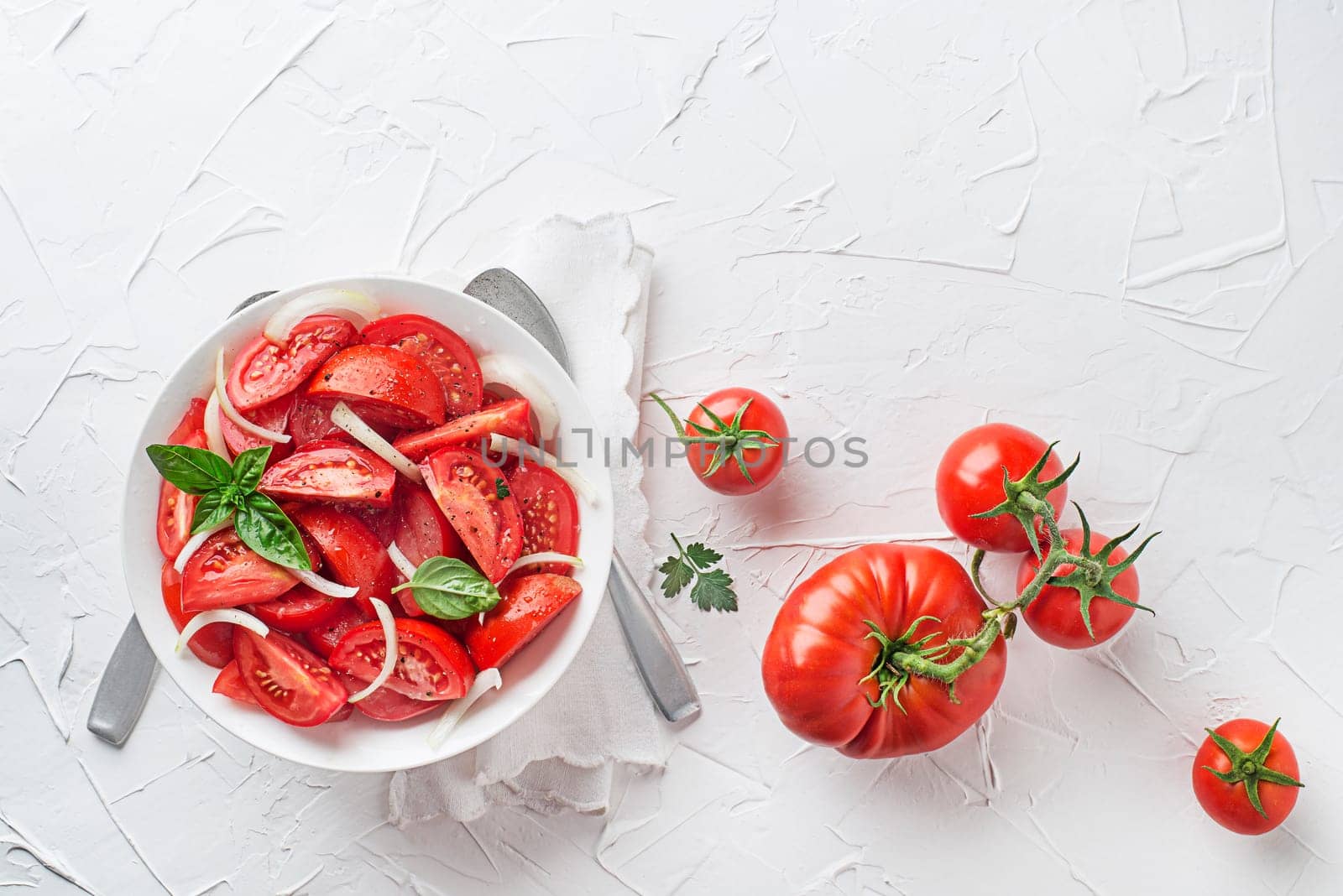 Fresh tomato salad with onion and basil on white table background. Concept for a tasty and healthy meal