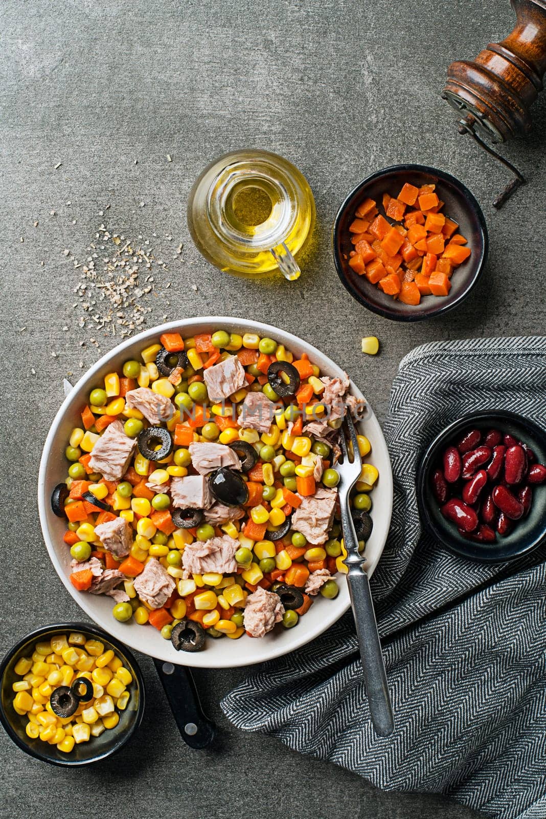 Healthy mixed tuna salad with corns, carrots, peas, beans and olives on grey table background. Mexican corn salad.