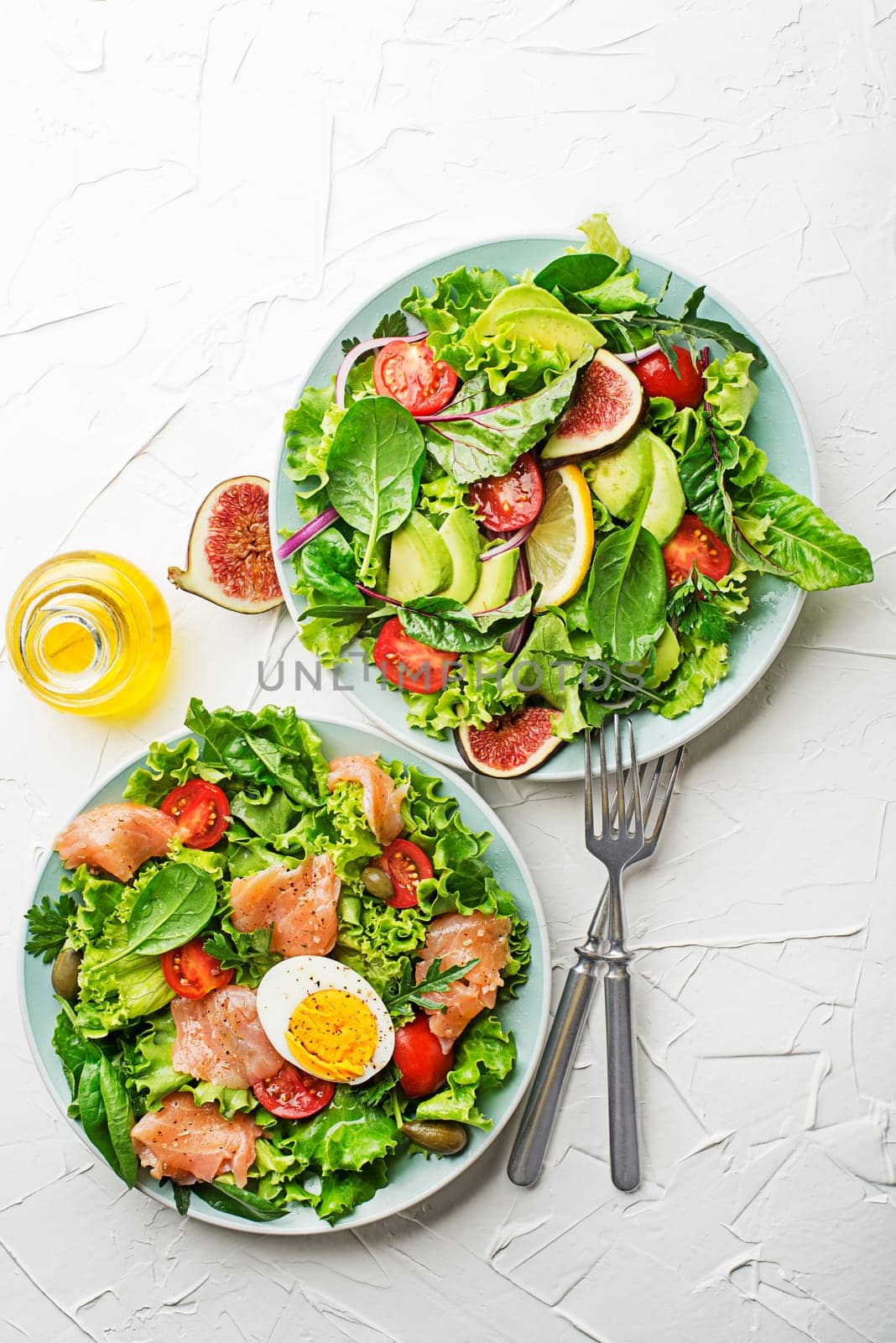 Fresh green lettuce salads with smoked salmon, cherry tomatoes, egg and avocado on white table background