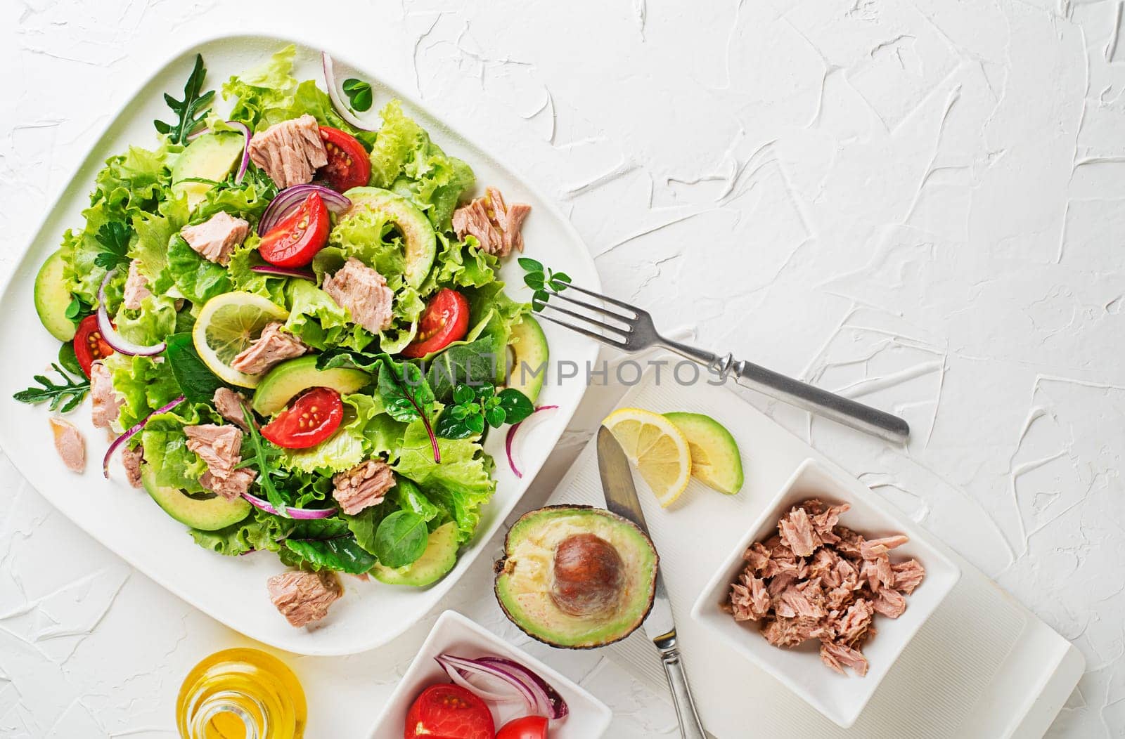 Fresh green leafy salad with tuna avocado and tomato on white table background. Concept for a tasty and healthy meal