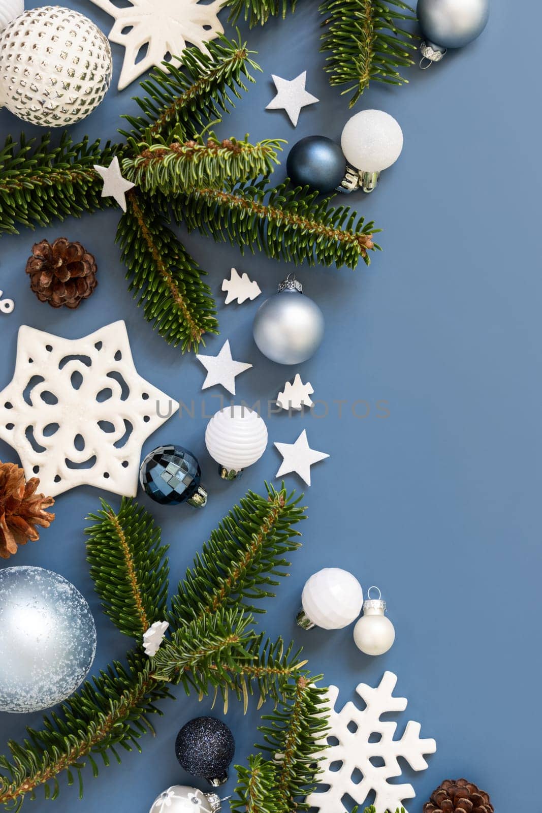 White Christmas decorations and fir tree branches on a blue top view with copy space. New Year and Christmas holiday atmospheric flat lay with baubles, snowflakes and stars