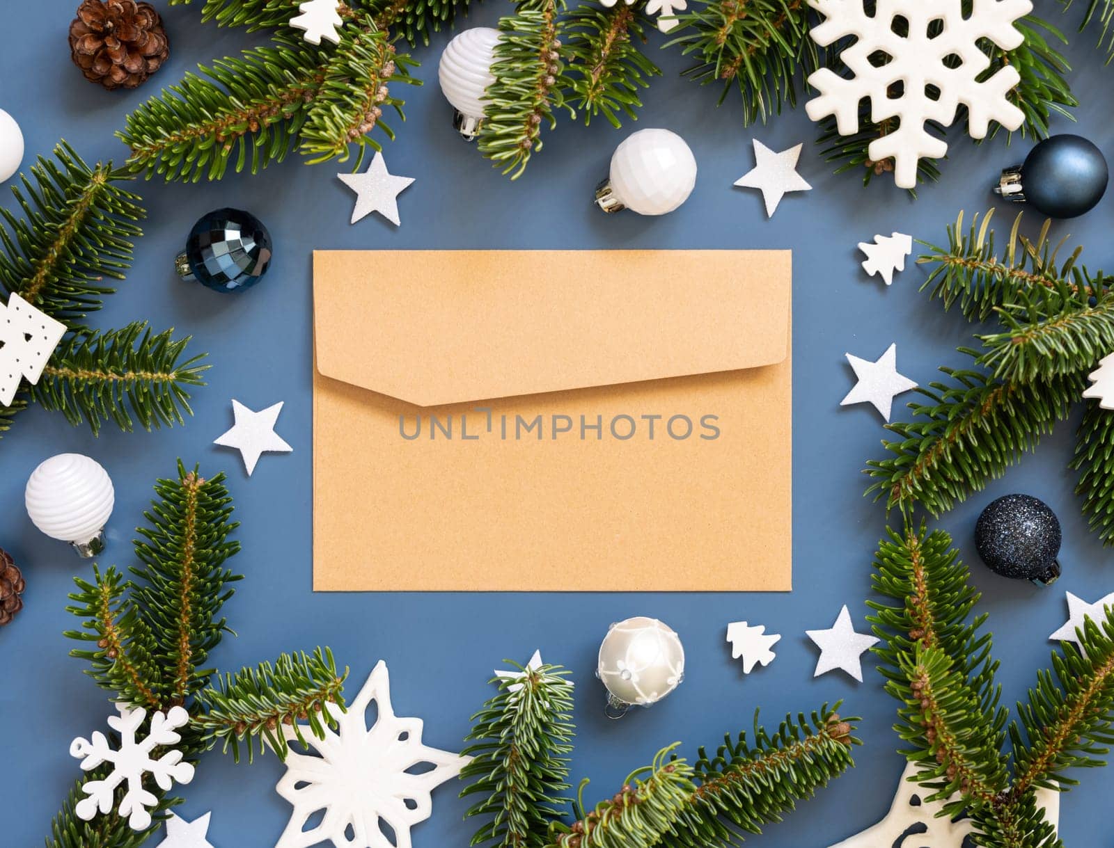 Craft paper envelope on a blue background near white Christmas decorations and fir branches top view, mockup, copy space.. New Year and Christmas holiday atmospheric flat lay