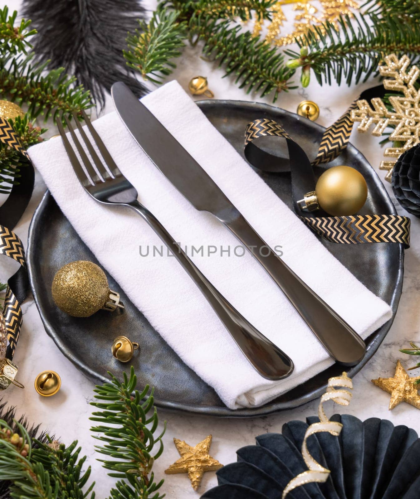 Black and golden Christmas table setting with decorations and fir tree branches close up. Winter table with fork, knife and plate. Winter New Year or Christmas dinner atmosphere