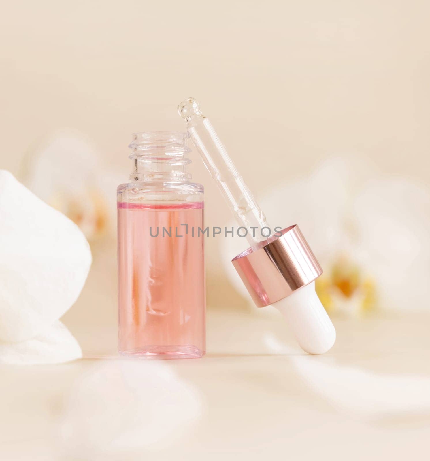 Light Pink opened Dropper Bottle with serum and a pipette cap near white orchid flowers on light beige, close up, copy space. Skincare cosmetic product, essence or serum. Everyday beauty routine.