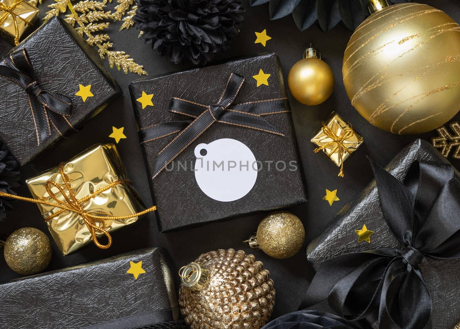 Black and golden Christmas Gift Boxes with a bow and ornaments close up, round paper gift tag mockup, copy space. Dark winter composition with blank label card for Christmas, New Year, Birthday, Anniversary