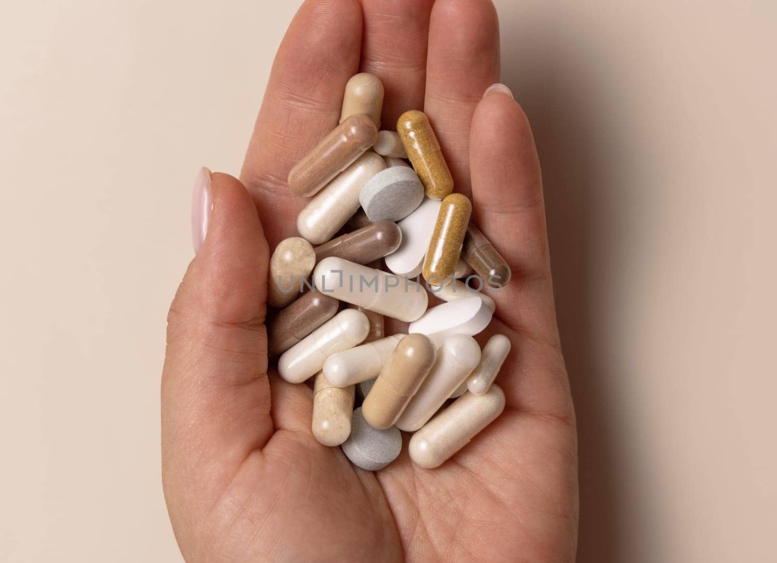 Hand with mix of medical capsules on light beige top view. Preventive medicine and healthcare, taking dietary supplements and vitamins. Assorted pharmaceutical medicine capsules