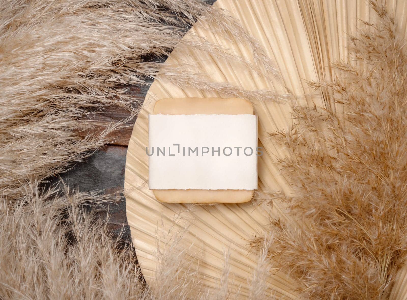 Handmade soap bar with blank label on dried palm leaf near pampas grass top view, mockup. Skincare beauty product. Bohemian eco friendly cosmetics flat lay with dried leaves.