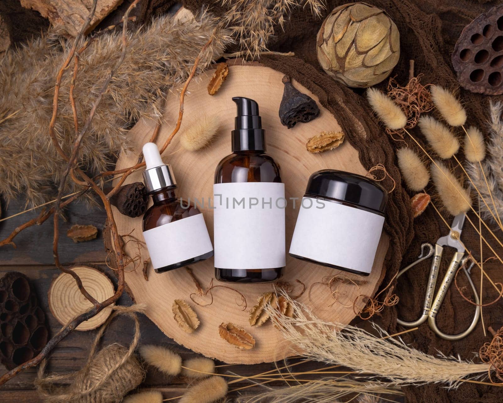 Refillable glass bottles on wood near natural boho decorations top view, label mockup. Skincare beauty product, lotion or essence. Bohemian eco friendly cosmetics flat lay with dried leaves.
