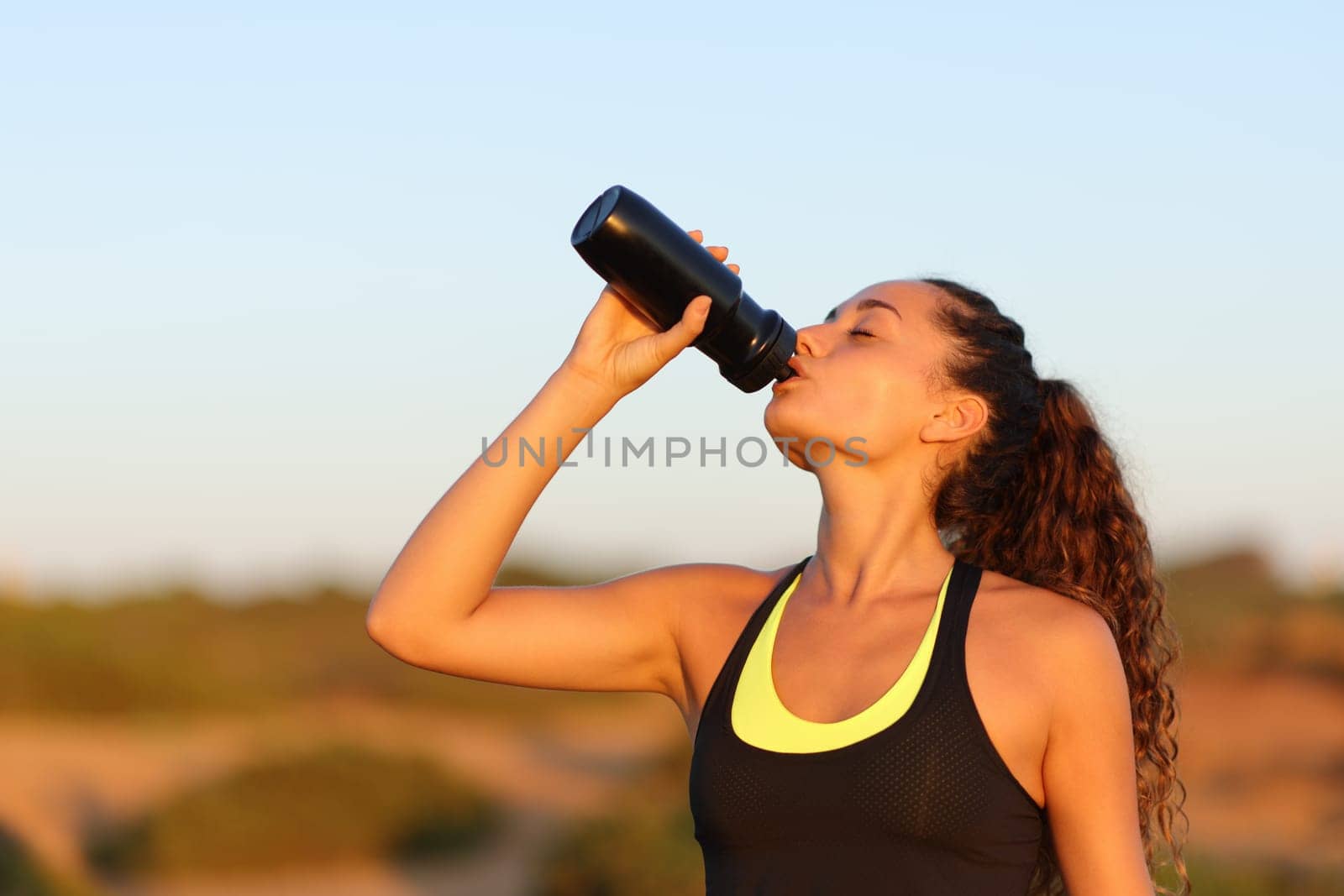 Runner drinking from bottle standing at sunset