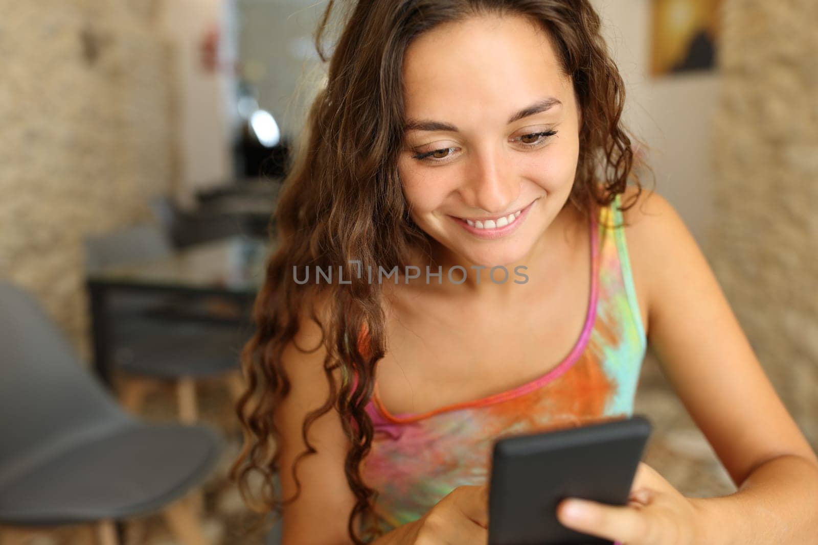 Happy woman in a bar using smart phone alone