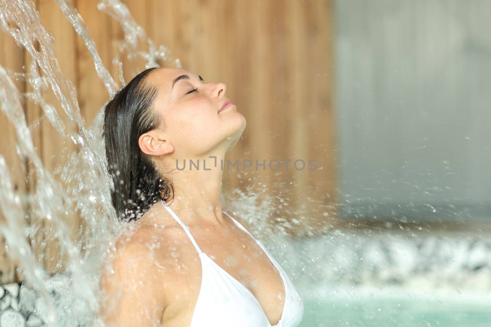 Relaxed woman in bikini breathing under water jet in spa pool