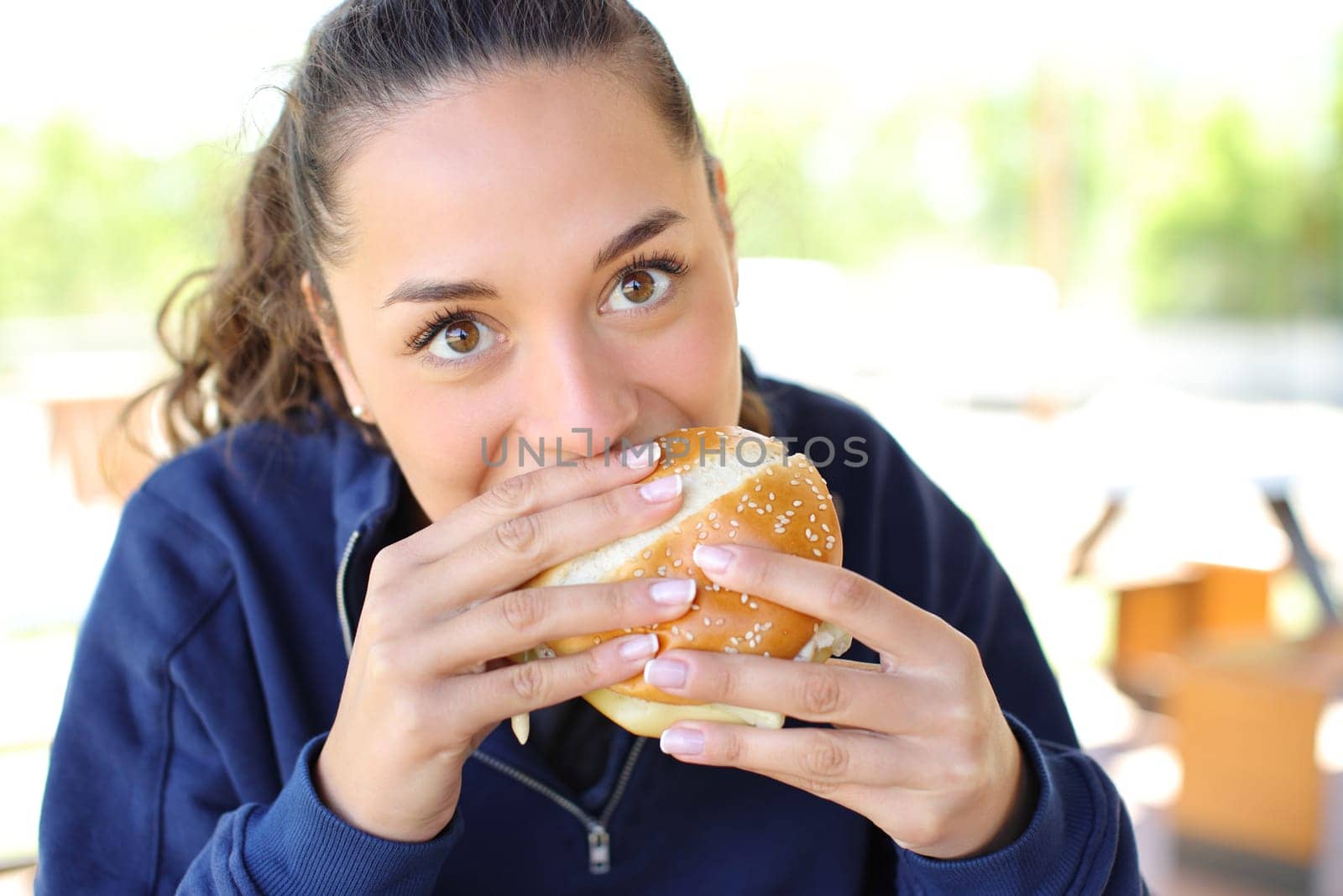 Front view portrait of a woman eating a burger looking at camera