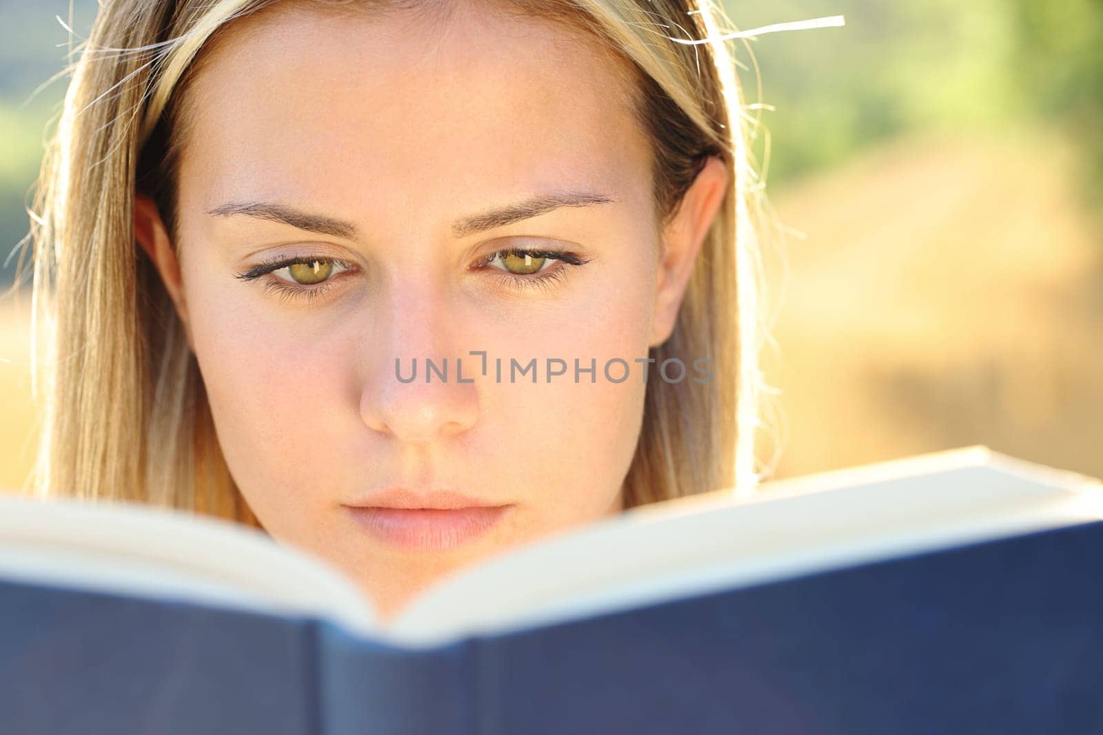 Front view close up portrait of a young woman reading a paper book in nature