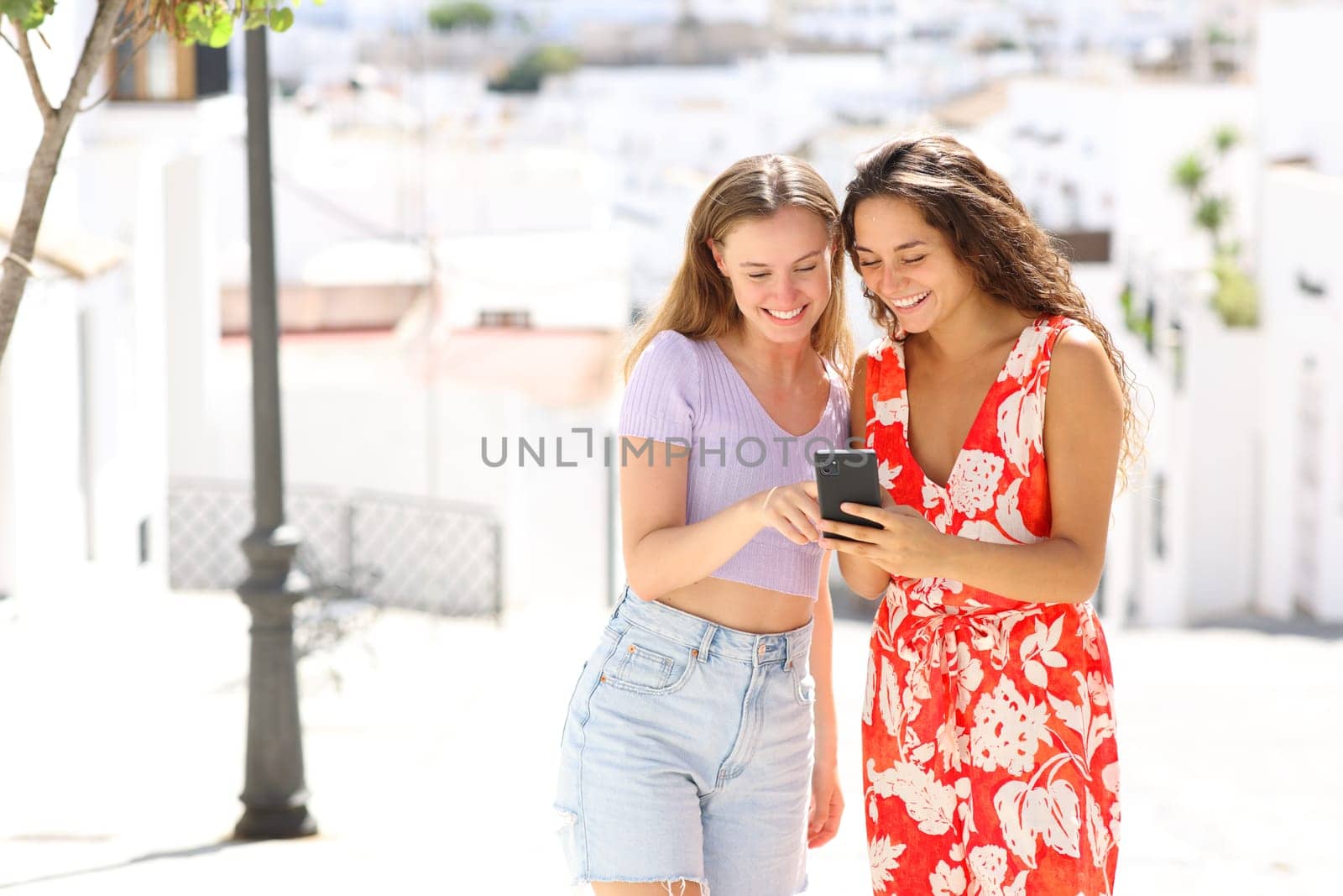 Happy tourists in a white town street checking smart phone on summer vacation