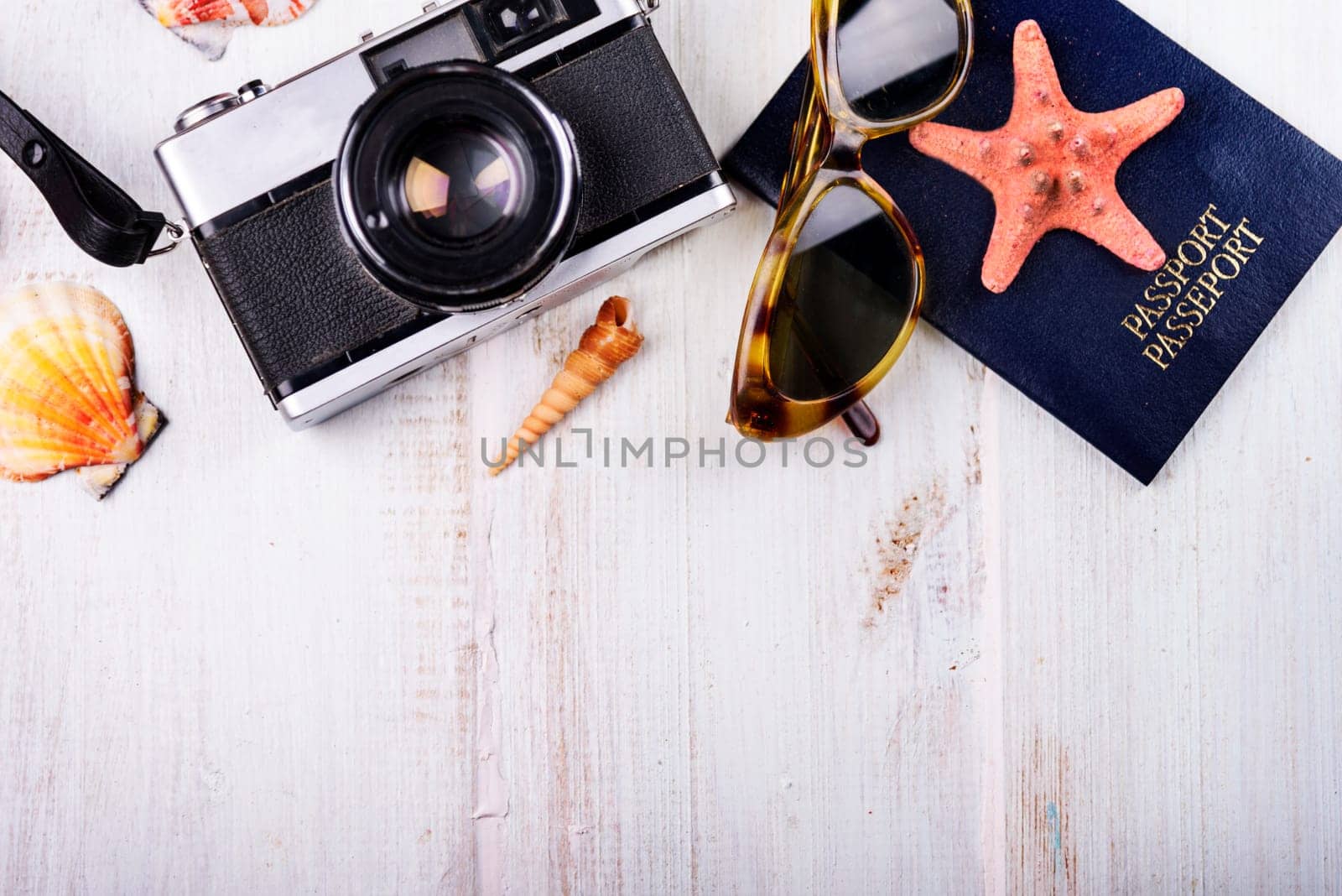 Vintage photo camera, passport, sunglasses and seashells border on wooden white background. Summer holiday design with copyspace. Traveling concept.