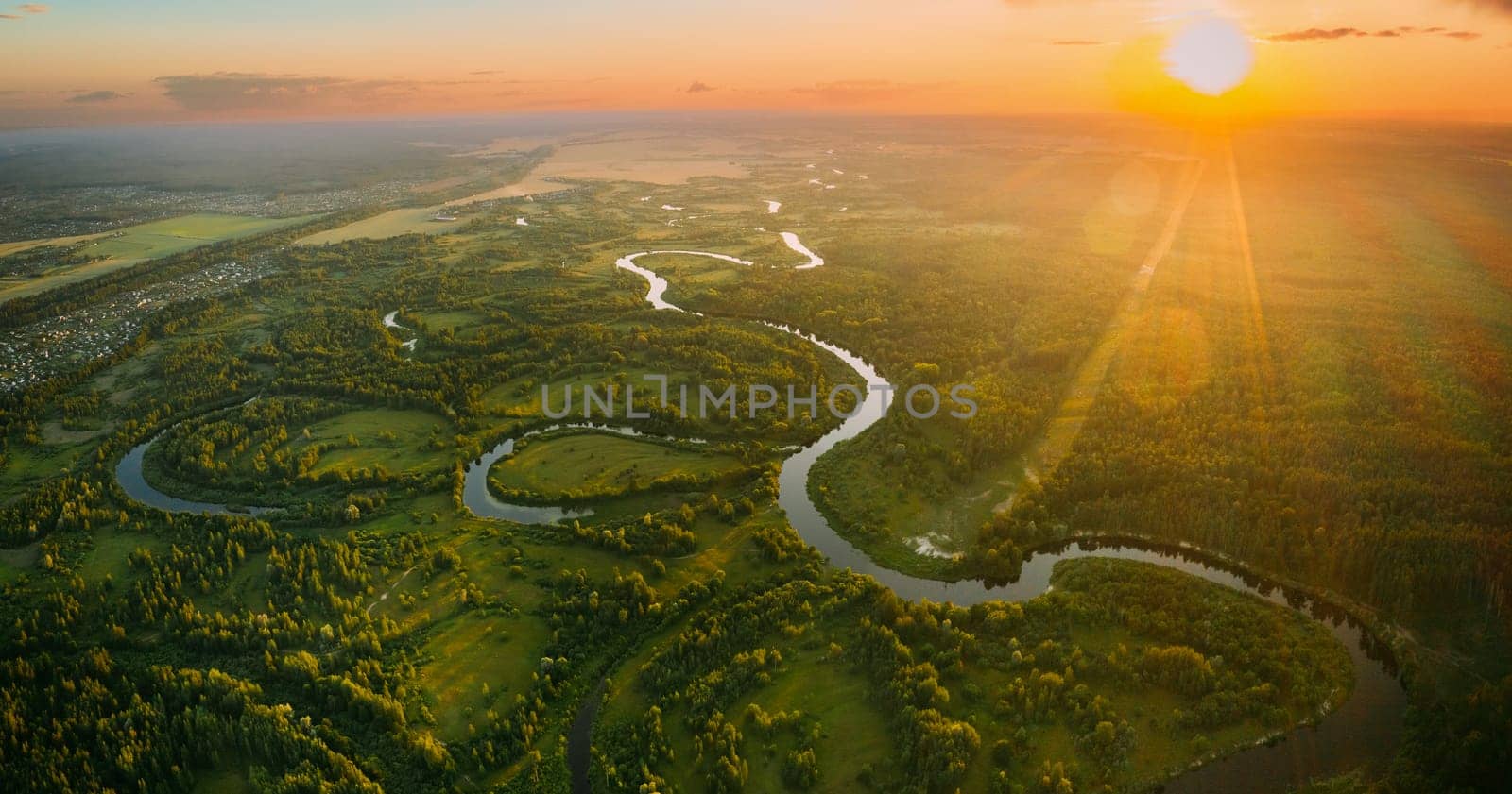 Aerial View. Beautiful Sunset Sun Sunshine Above Green Forest, Meadow And River Landscape In Sunny Evening. Top View Of European Nature From High Attitude In Summer Sunrise. Bird's Eye View. Panorama.