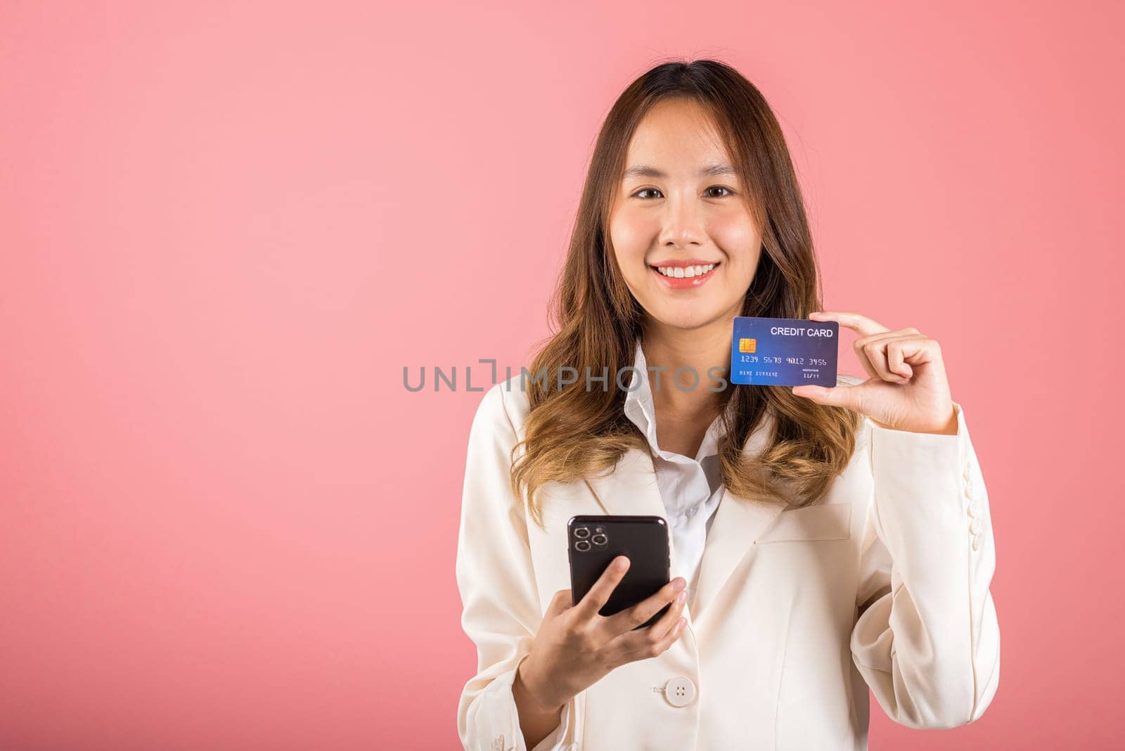 Happy Asian portrait beautiful cute young woman excited smiling hold mobile phone and plastic debit credit bank card, studio shot isolated on pink background, female using smartphone online shopping
