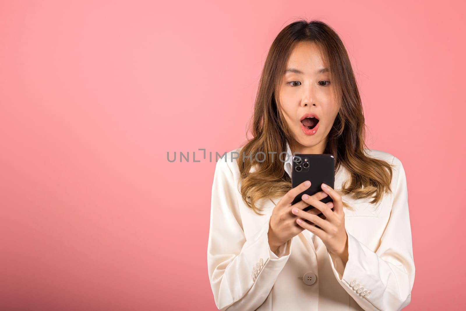 Asian happy portrait beautiful cute young woman teen smiling standing surprised excited wow gesture with smart mobile phone looking smartphone studio shot isolated pink background with copy space