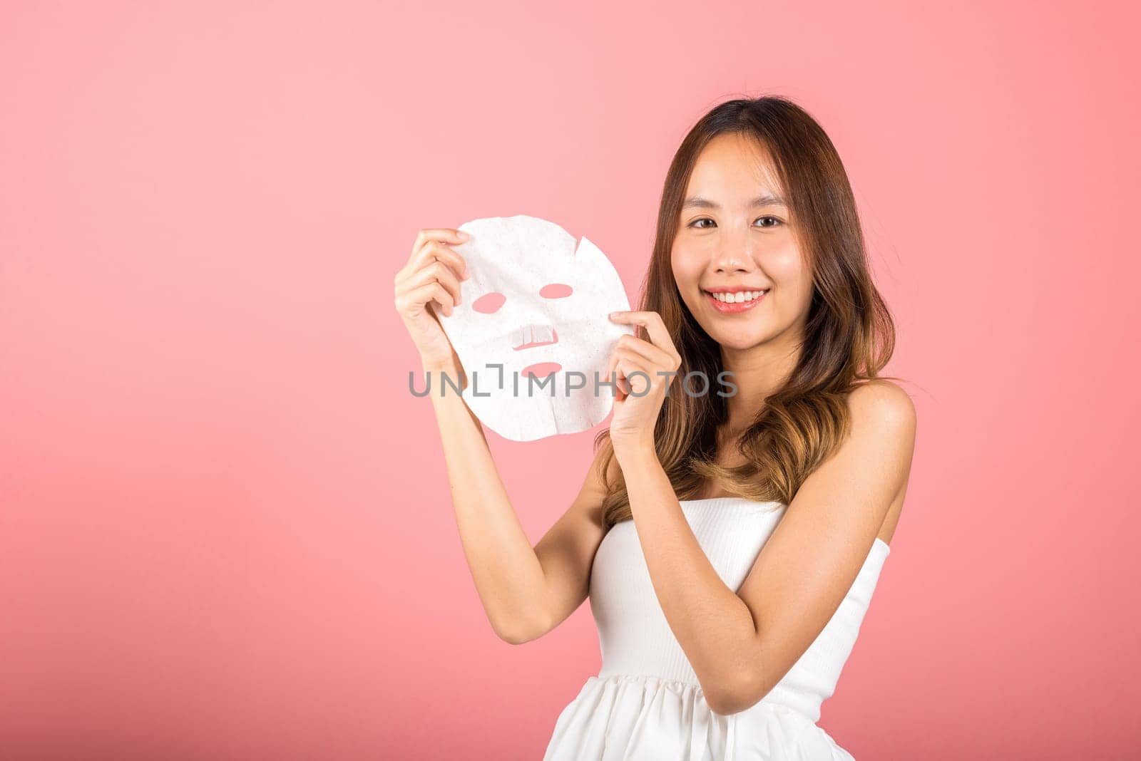 Healthcare spa. Portrait beautiful female smiling holds facial sheet mask, Studio shot isolated on blue background, Asian woman holding purifying mask face on hands, Skin care healthcare cosmetic