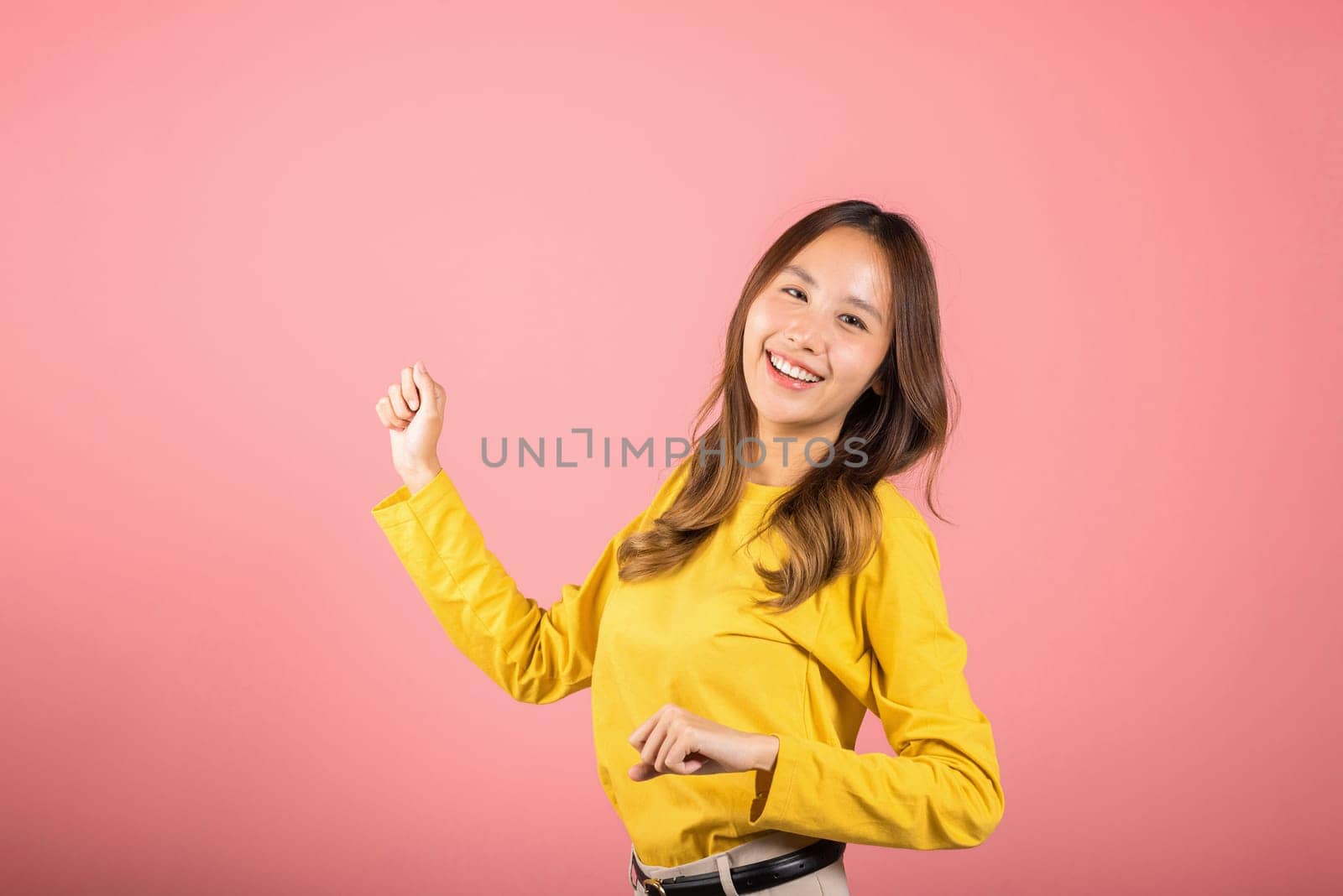 Asian young woman dancing with inspired face expression and raising hands up, Portrait of happy female model jocund in sneakers dancing, studio shot isolated on pink background, Time to relax