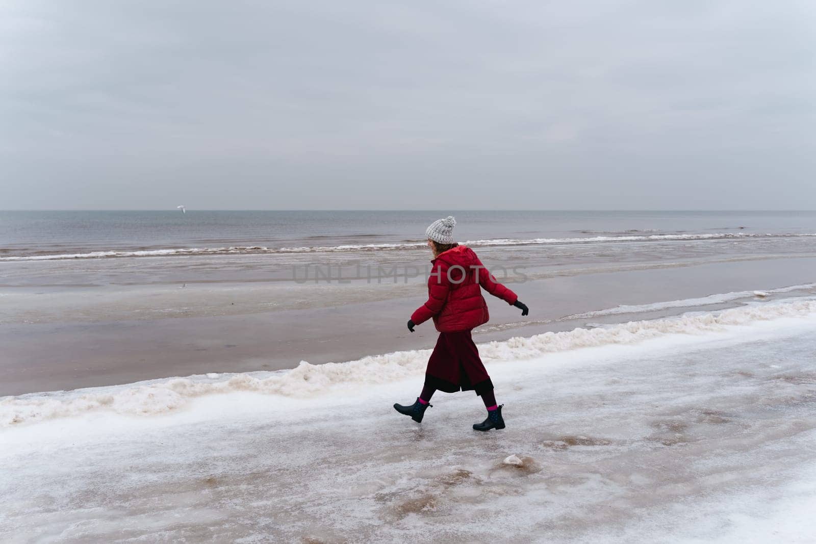 A woman in red walks in winter along the seashore.
