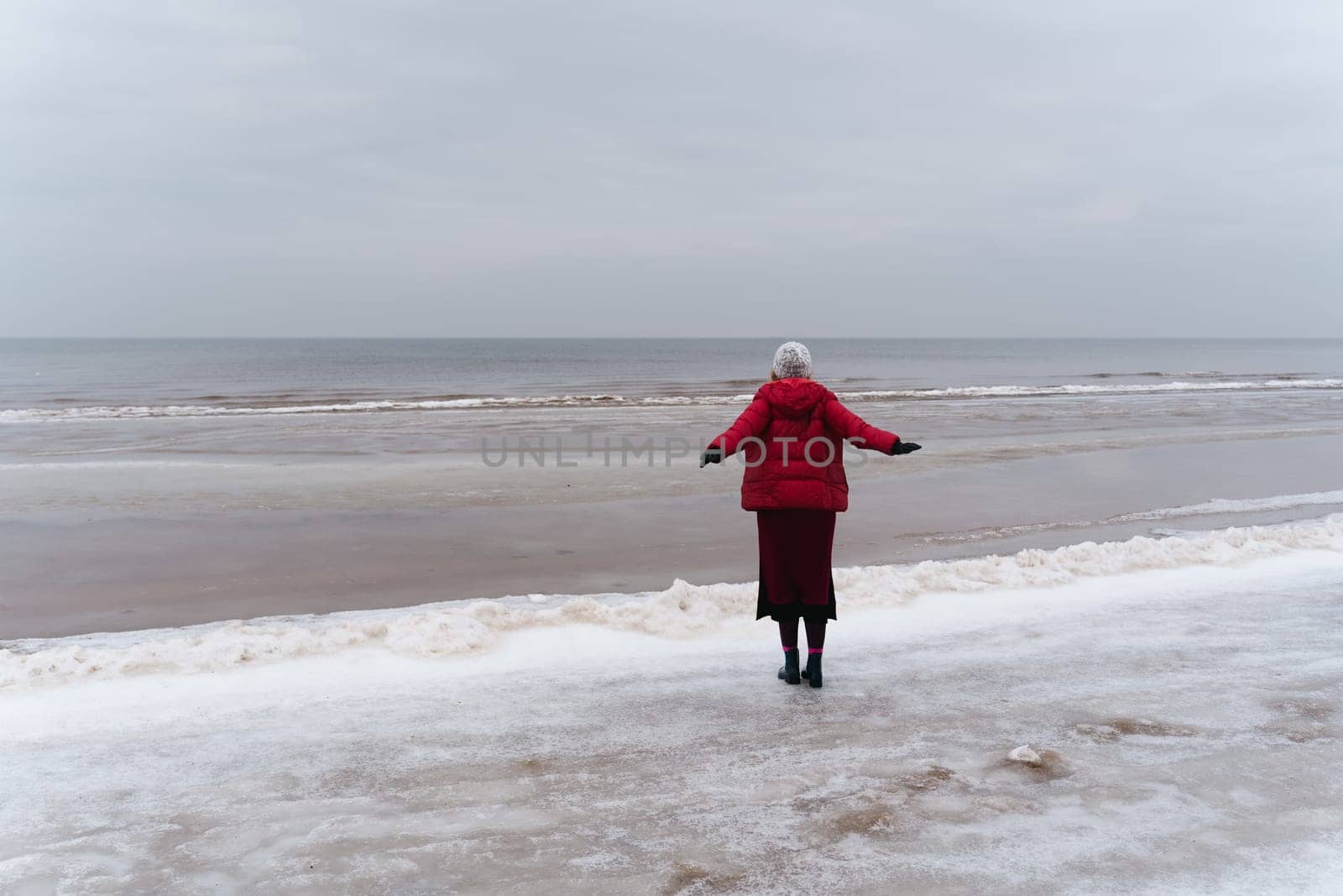 A woman stands looking at the sea spreading her arms to the sides, the view from behind.
