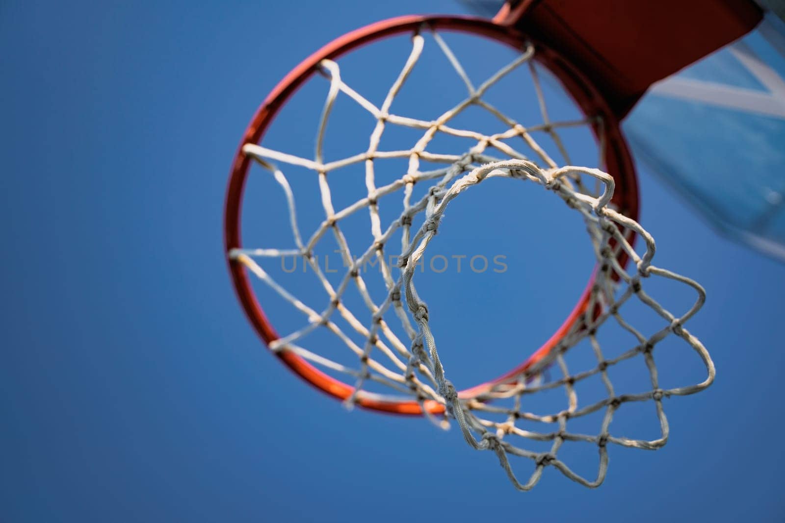 closeup of outdoor basketball basket net of white rope view from underneath against a blue sky with copyspace
