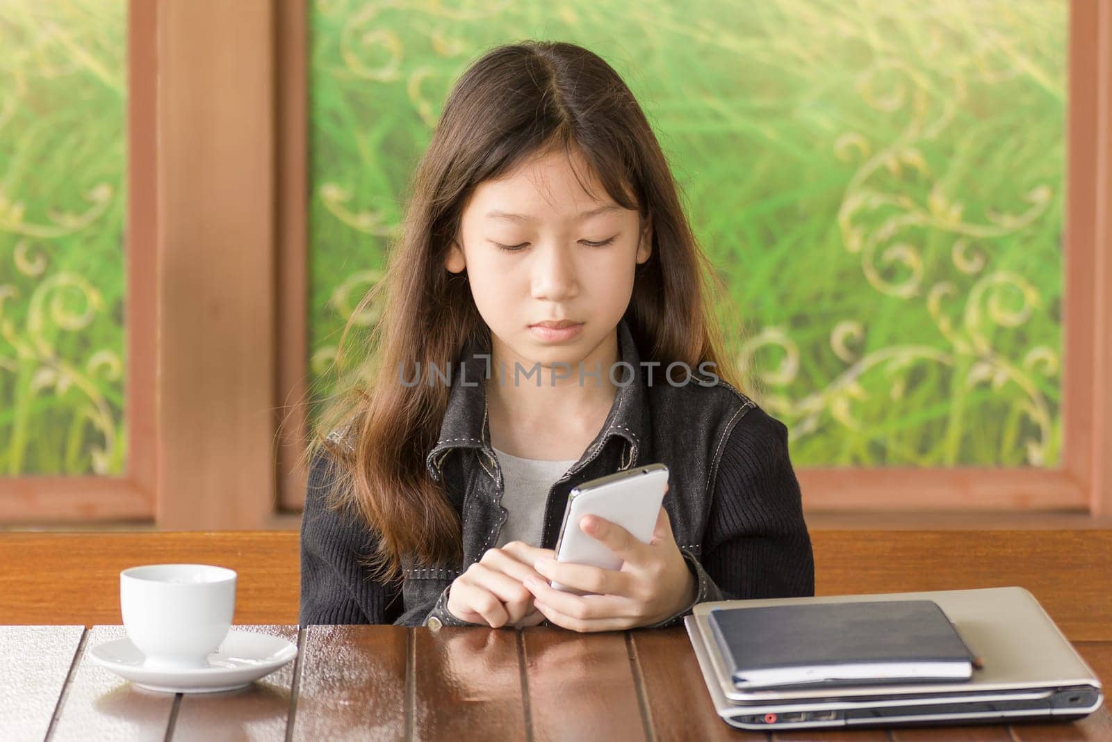 Asian young girl using mobile phone while sitting at desk