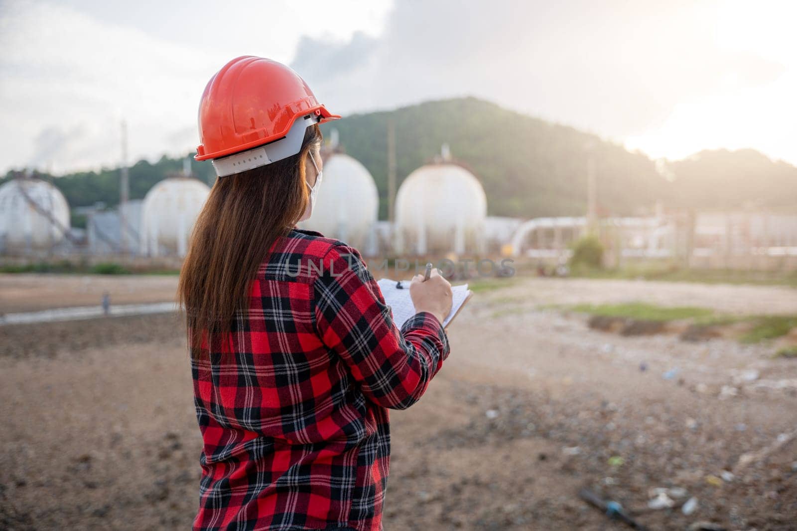 Petroleum Engineers. Happy Asian worker woman in oil chemical industry working visual inspection list on clipboard in plant, do Action of worker standing write safety checklist which is clipped