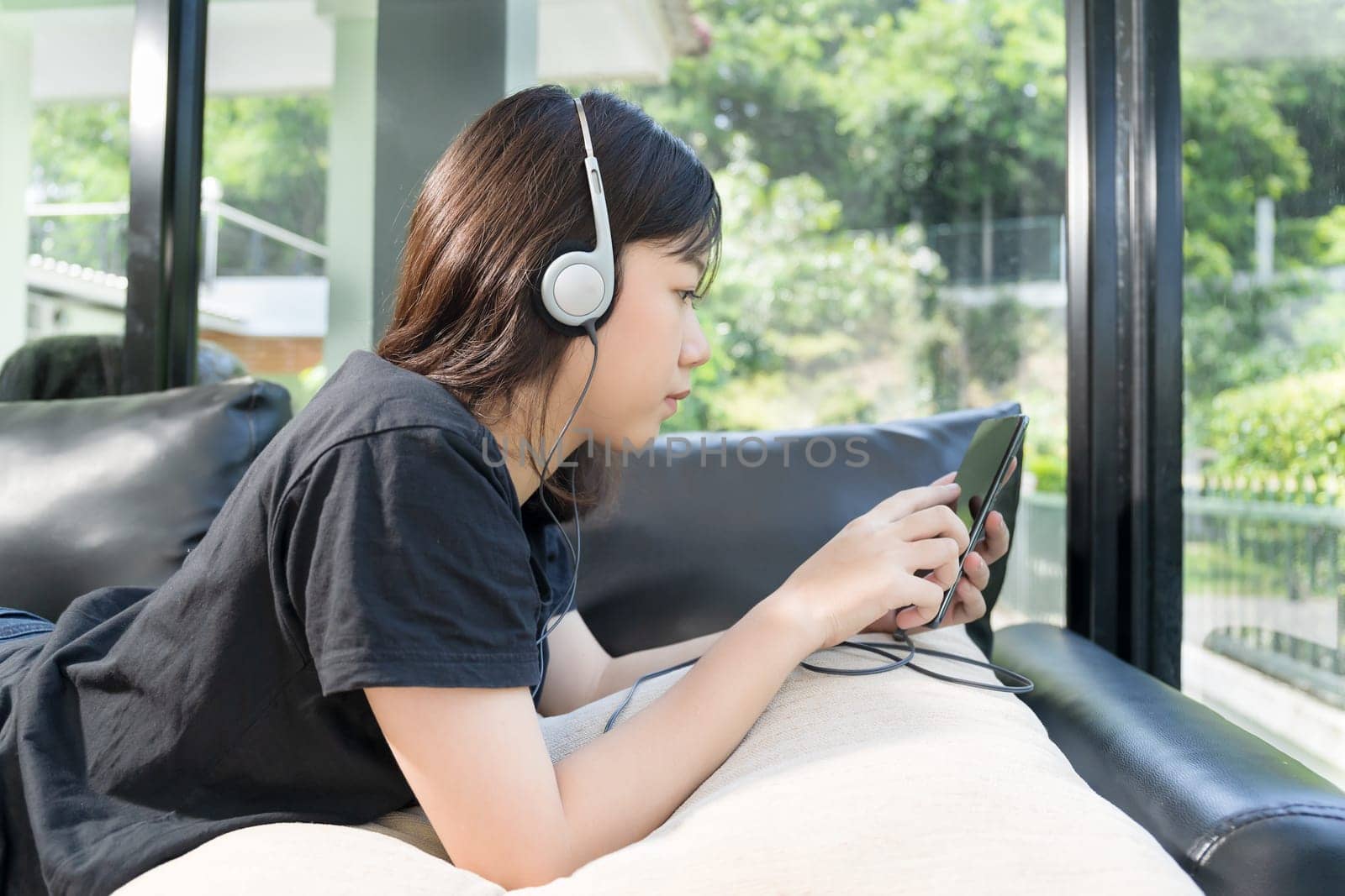 Young girl with headphones and listening to music from mobile phone on the sofa in living room at home
