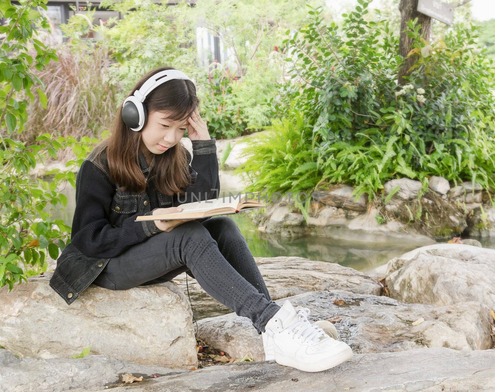 Young beautiful girl reading a book and .listen to music at the park