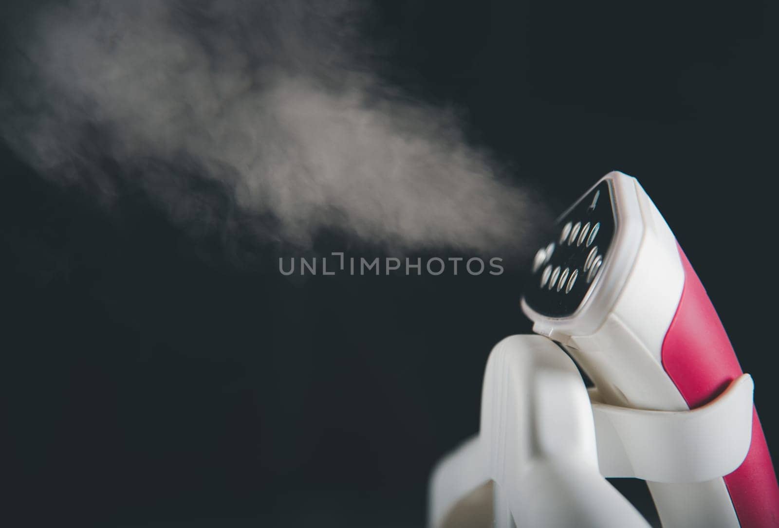 Close up of electric hand steam generator while it's hot and steam comes out on the ironing board place for clothes on black background, Household & home equipment for housework, concept of linen care