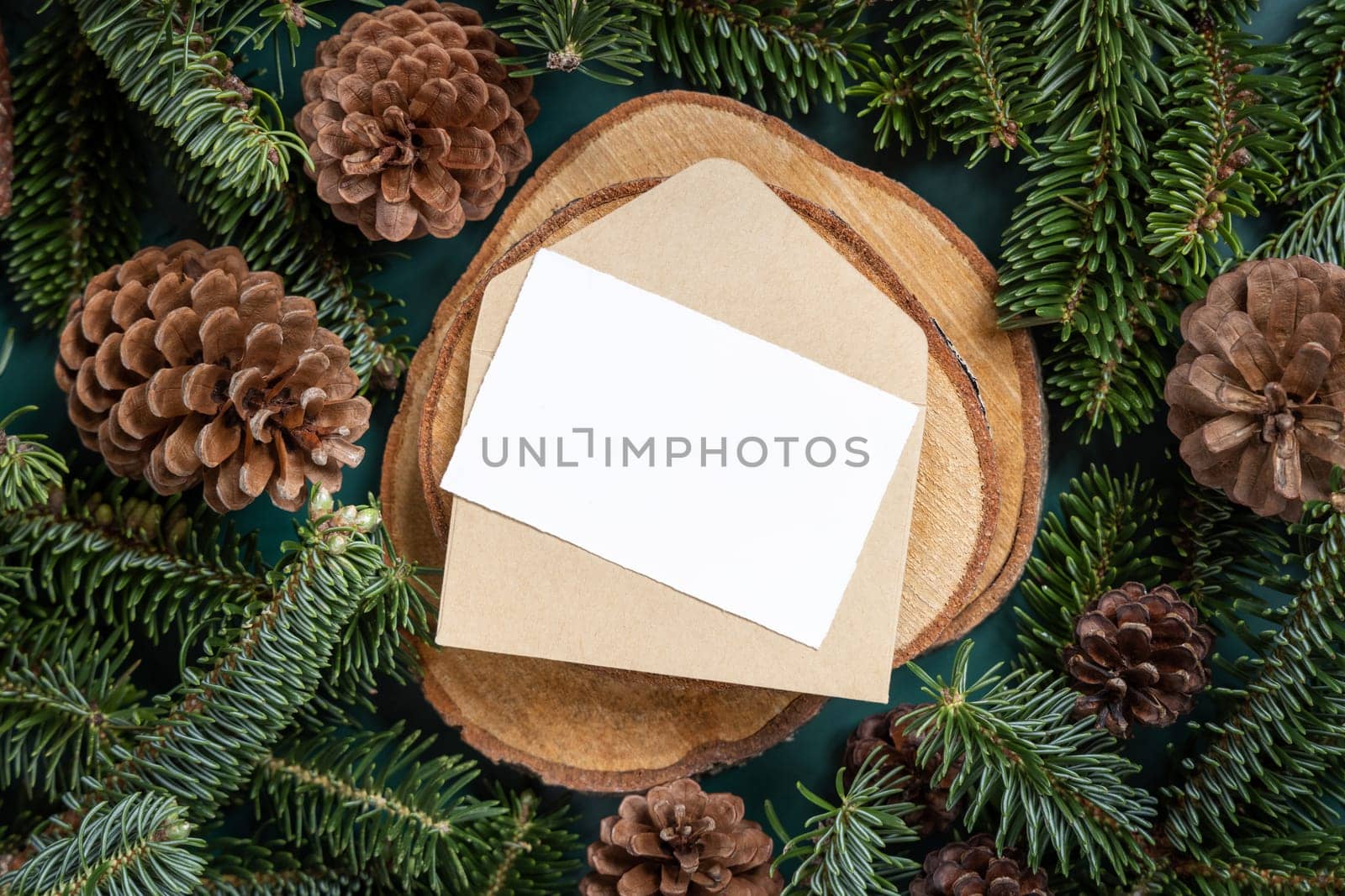 Horizontal blank card and envelope between fir branches and pine cones on green close up, mockup. Christmas or New Year greeting card template, Holiday winter composition