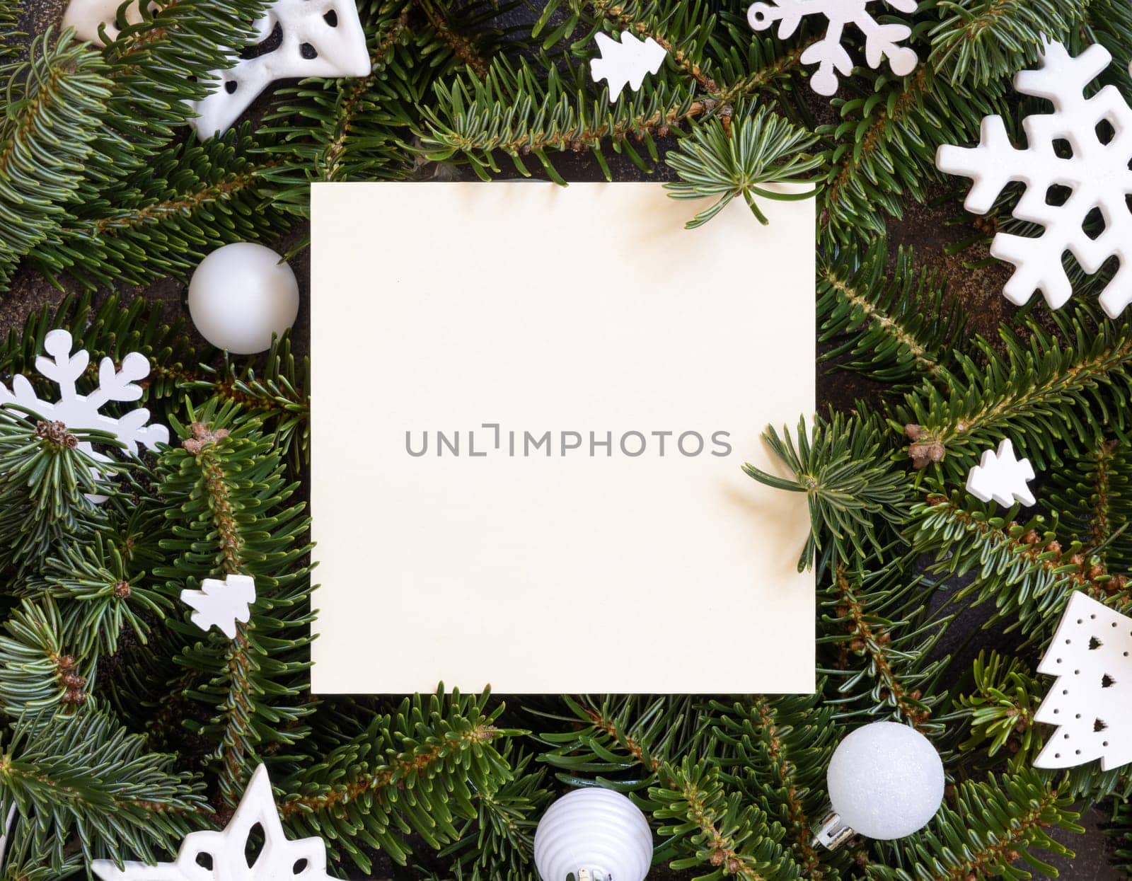 Blank card between white Christmas decorations and green fir branches top view. Square card mockup, flat lay, copy space. Christmas or New Year greeting card template, Holiday stationery