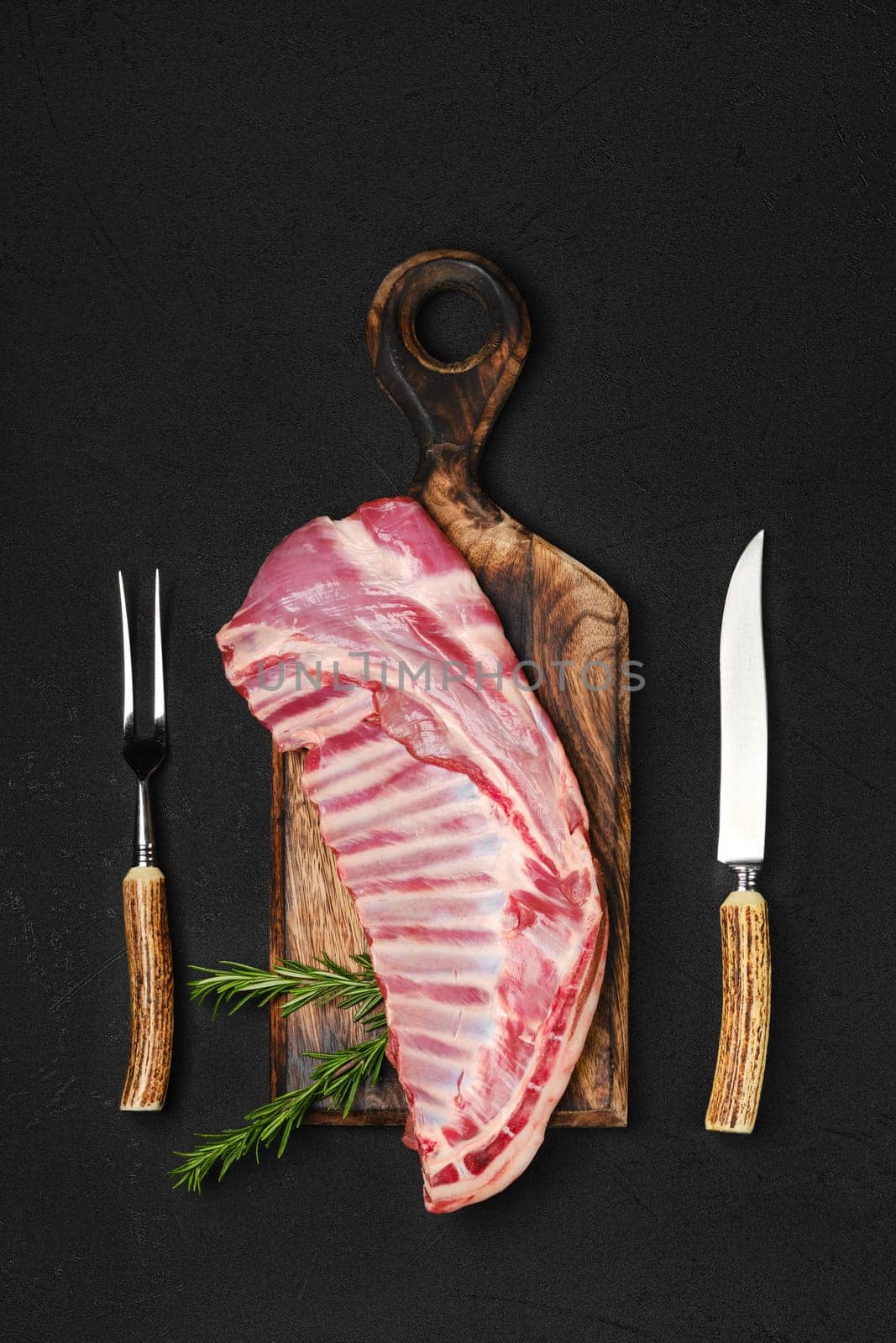 Top view of raw fresh lamb ribs, uncut with fork and knife for grilling