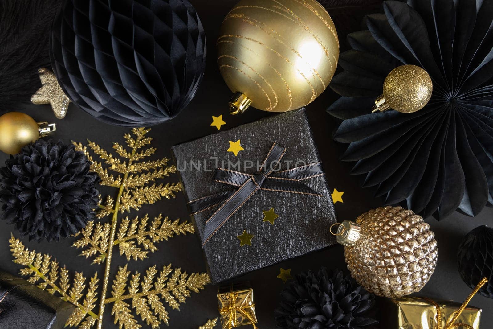 Christmas Gift Box with a bow near black and golden ornaments and baubles top view. Dark winter flat lay for Christmas, New Year, Birthday, Anniversary
