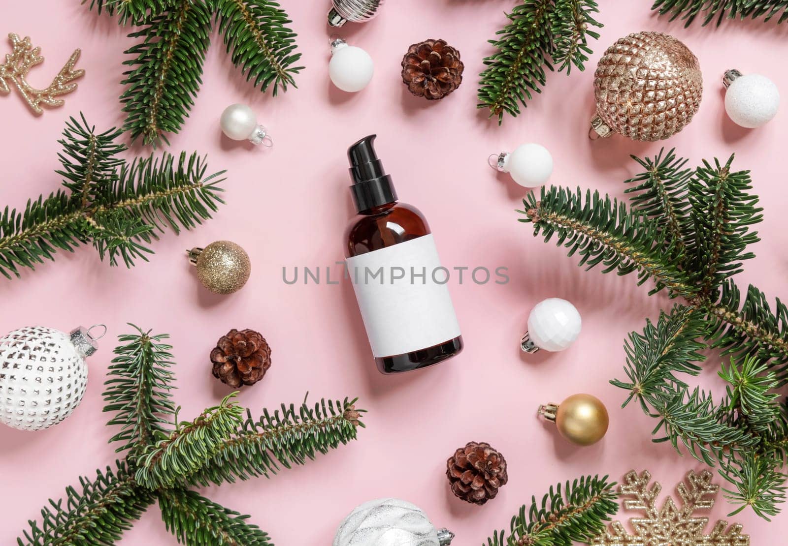 Brown glass one pump Bottle near Christmas decorations, fir branches and pine cones on pink top view. Holiday brand packaging mockup. Skincare beauty product, cream or serum. Healthcare natural cosmetics