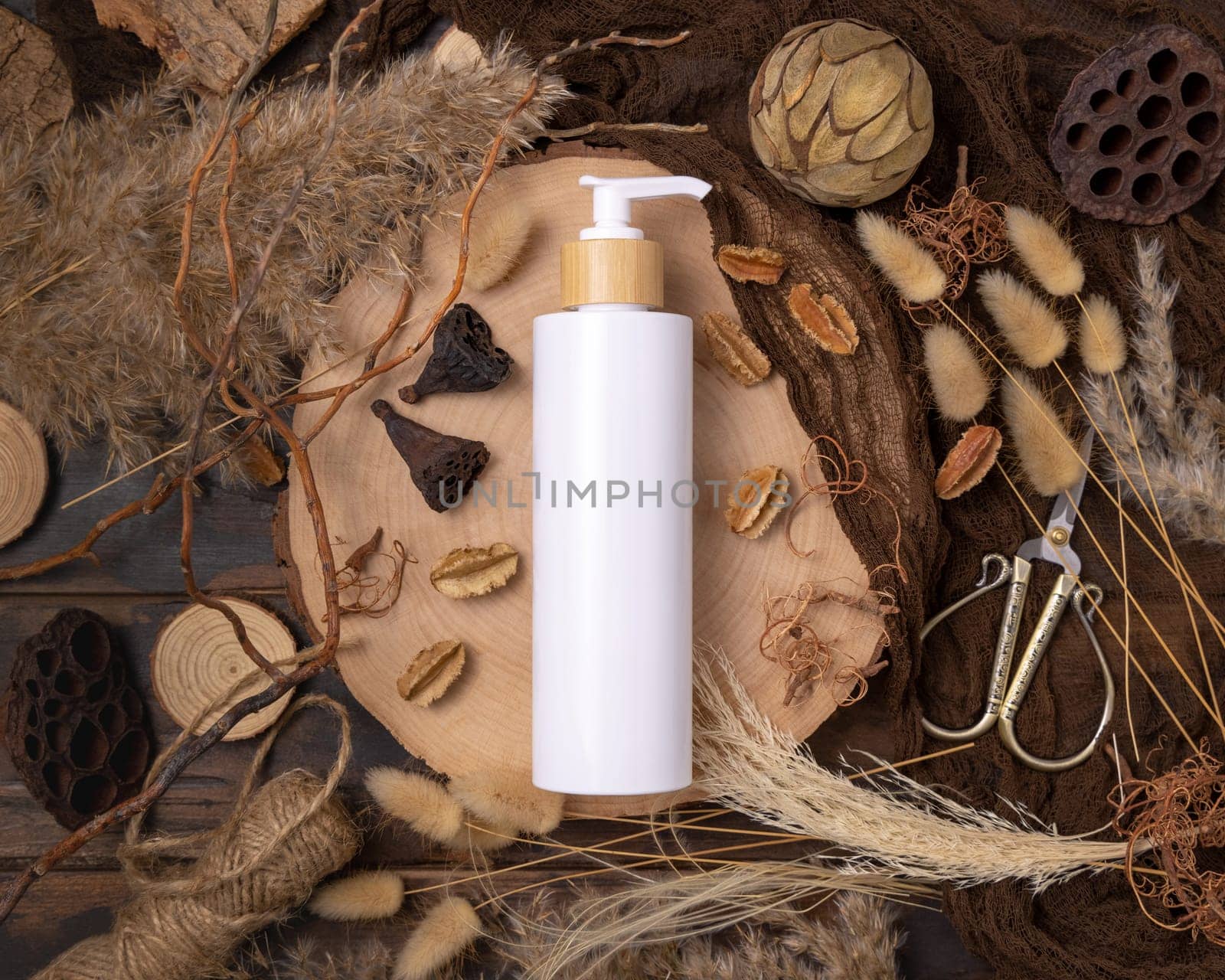 Refillable white one pump bottle on wood near natural boho decorations top view, label mockup. Skincare beauty product, lotion or essence. Bohemian eco friendly cosmetics flat lay with dried leaves.