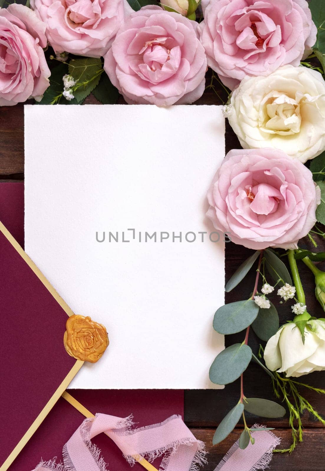 Card and red envelope between pink and cream roses on brown wood top view, wedding mockup. Romantic scene with cards, envelope and pastel flowers flat lay. Valentines, Spring or Mothers day concept
