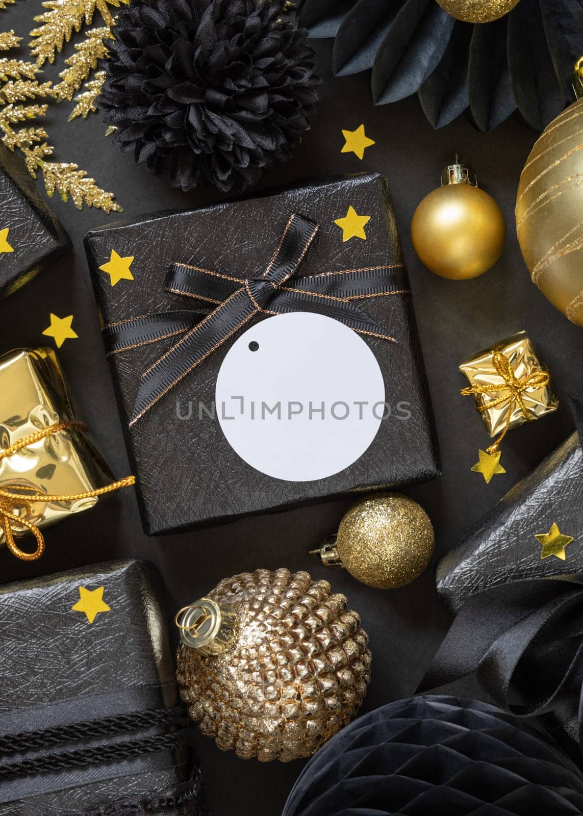 Black and golden Christmas Gift Boxes with a bow and ornaments close up, round paper gift tag mockup, copy space. Dark winter composition with blank label card for Christmas, New Year, Birthday, Anniversary