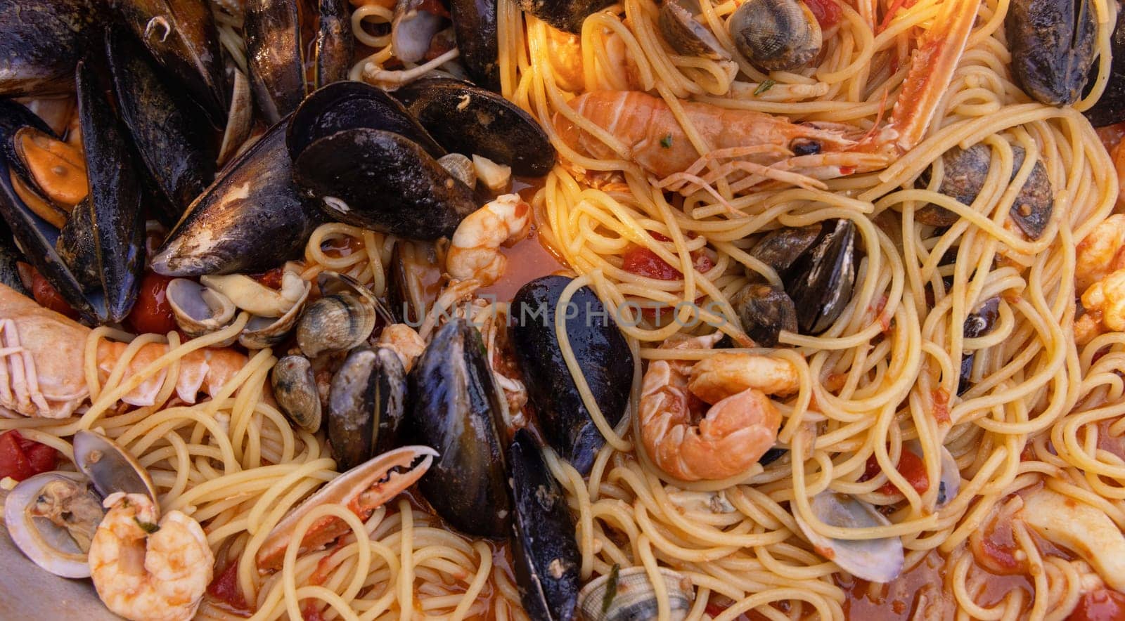 Italian spaghetti allo scoglio, pasta with seafood and tomatoes close up in a frying pan. Mediterranean Apulian traditional food with fresh stewed clams, shrimps, mussels, scampi, octopus and squid
