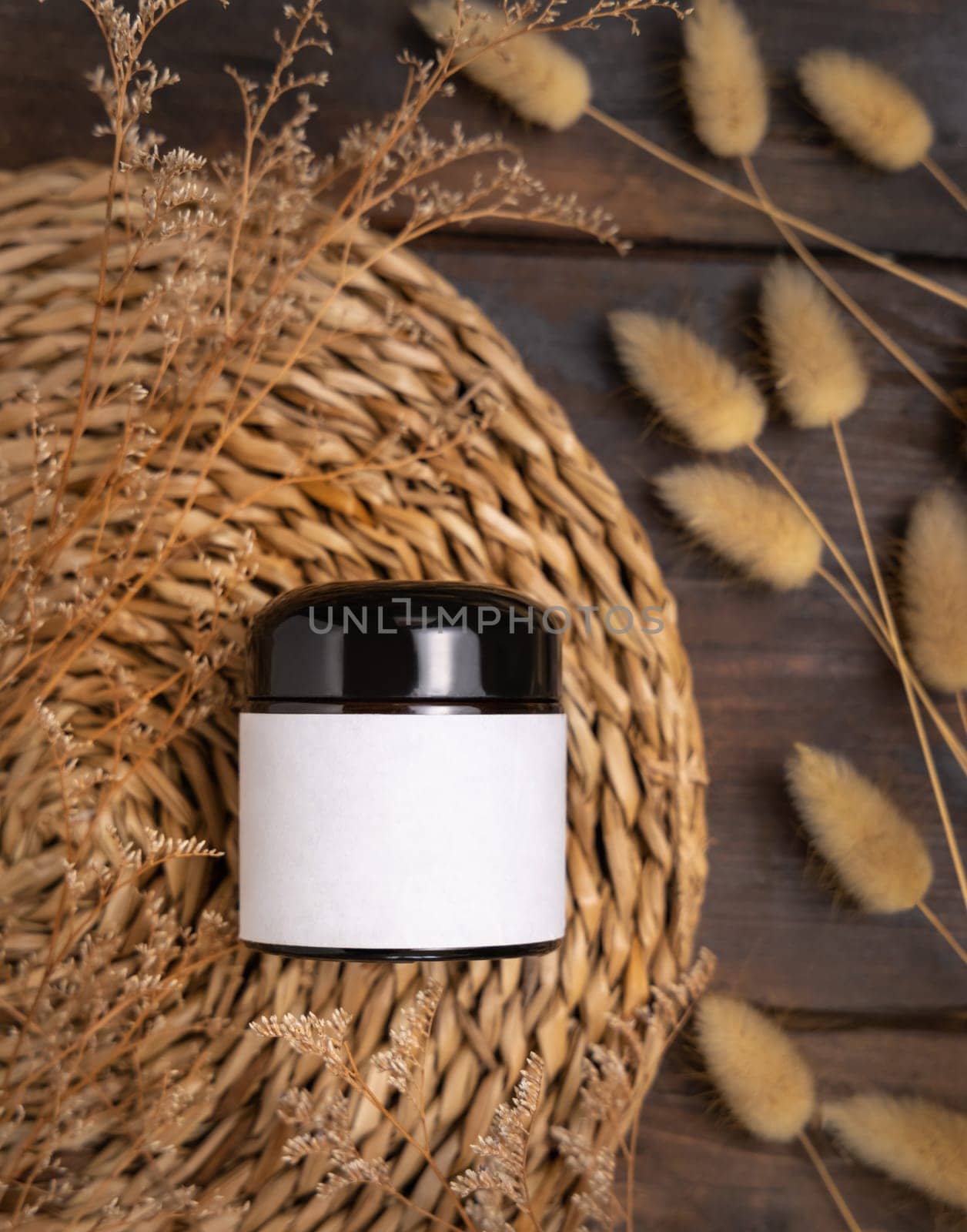 Cream jar on wattled boho placemat on wood near Hare's Tail grass top view, packaging label mockup. Natural skincare product for everyday beauty routine. Bohemian eco friendly cosmetics flat lay.