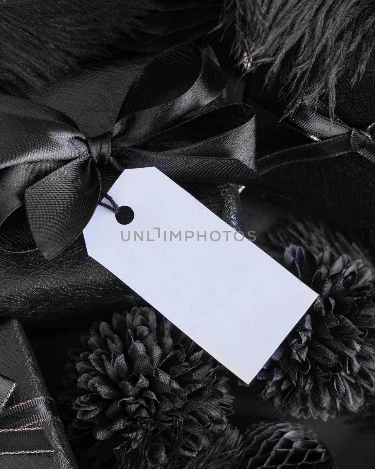Wrapped Gift Boxes with black paper flowers and decorations and rectangular gift tag, mockup, copy space. Dark composition with blank label card for Birthday, Anniversary or black party present